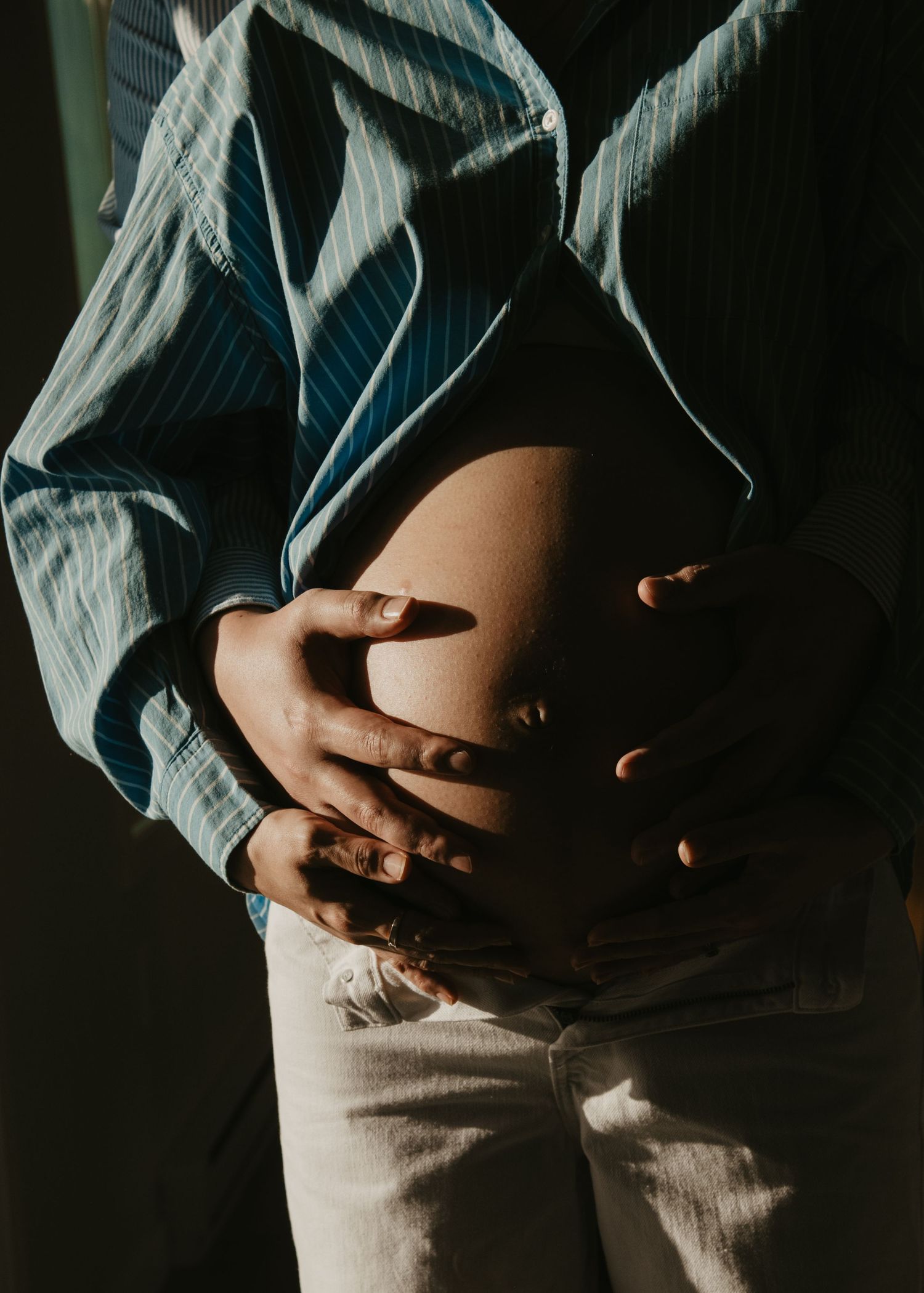 Artistic maternity photo showing hands cradling a pregnant belly in moody lighting. Calgary Maternity Photographer