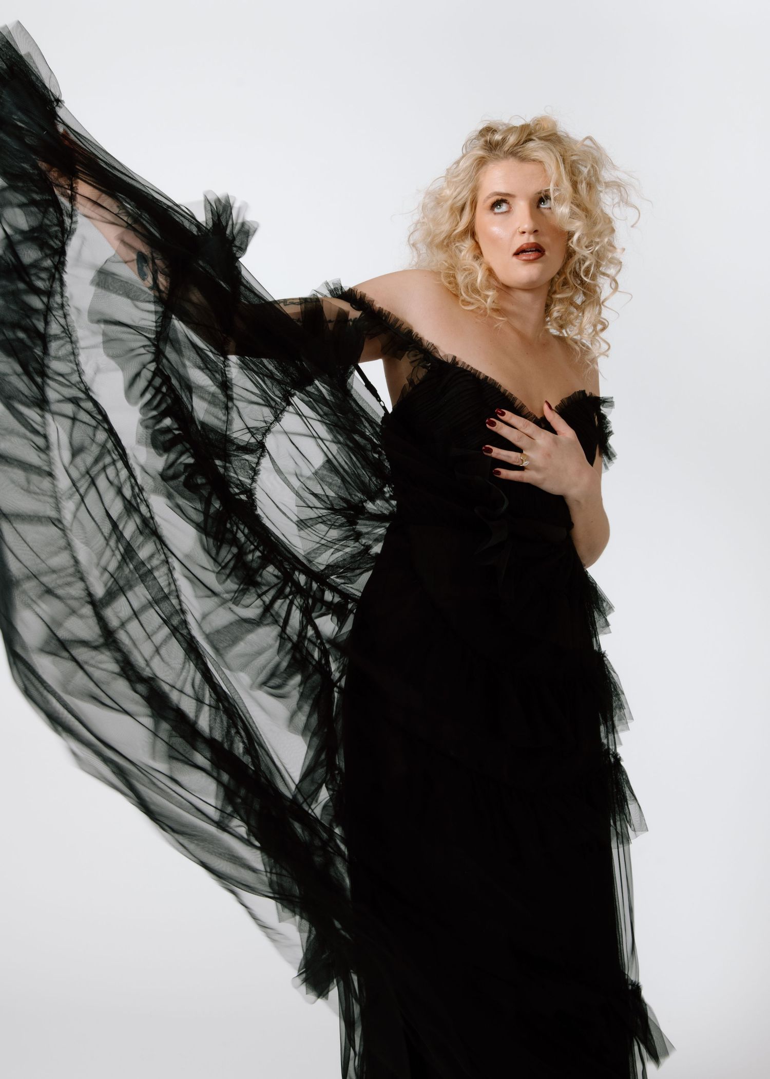 Model in dramatic black gown with flowing fabric poses against white background. Calgary Alberta Branding Photographer.