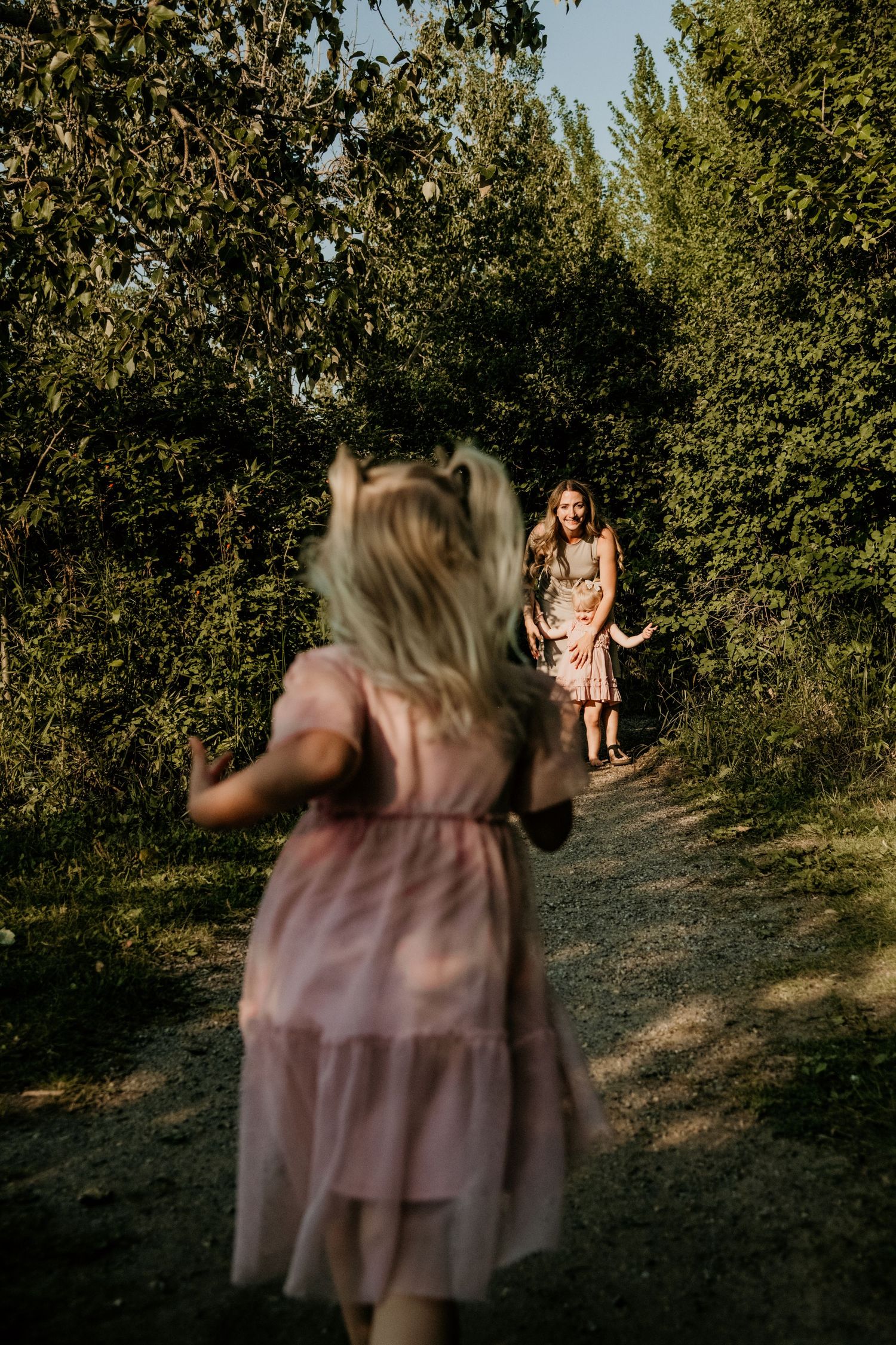 Two people in flowy dresses share a moment on a tree-lined path. Calgary Alberta Family Photographer.