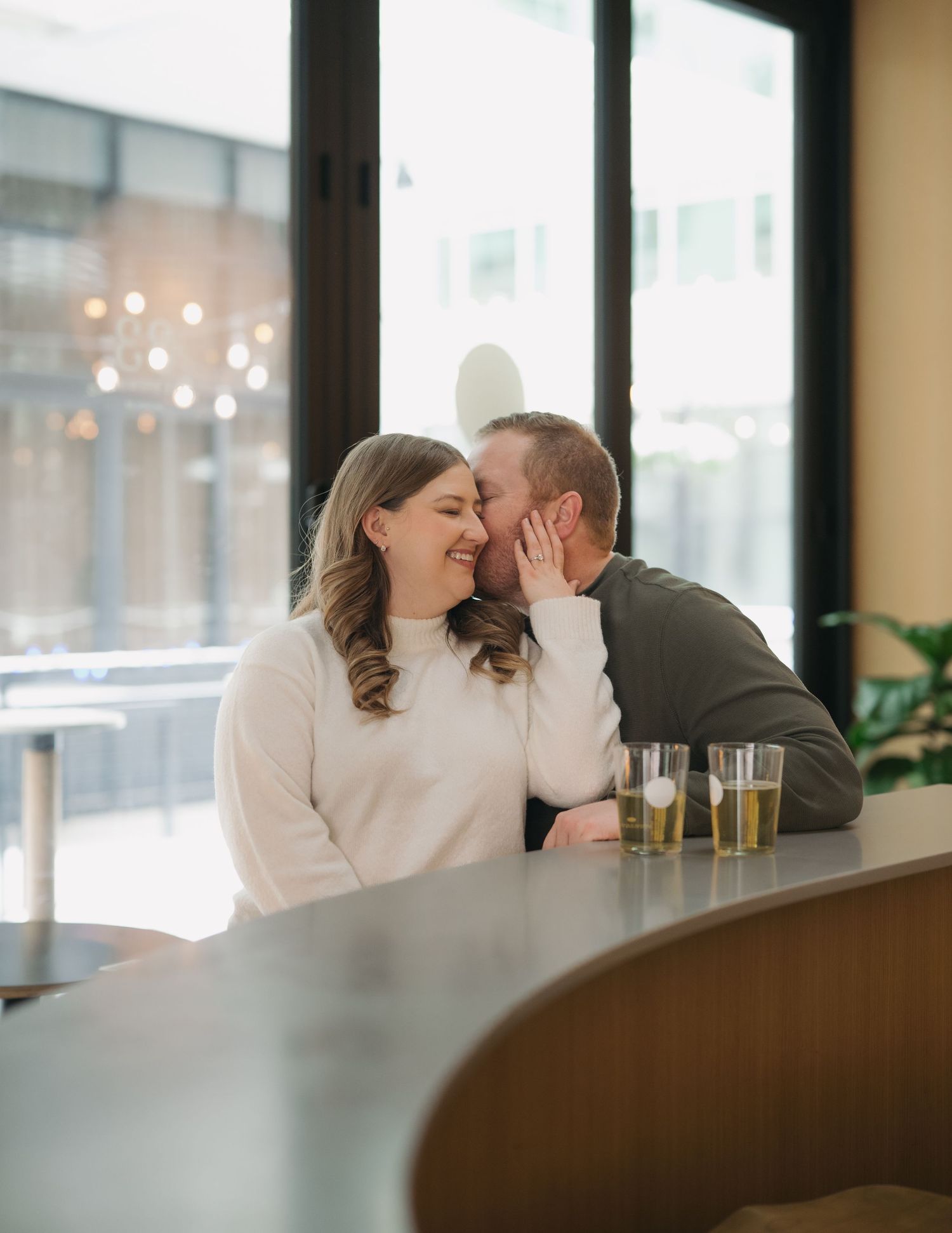 A couple sharing an intimate moment while sitting at a restaurant booth with drinks on the table.