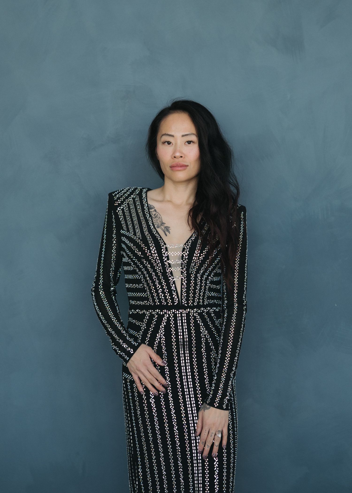 A figure poses in a sparkly black and silver striped long sleeve gown against a blue-grey backdrop.