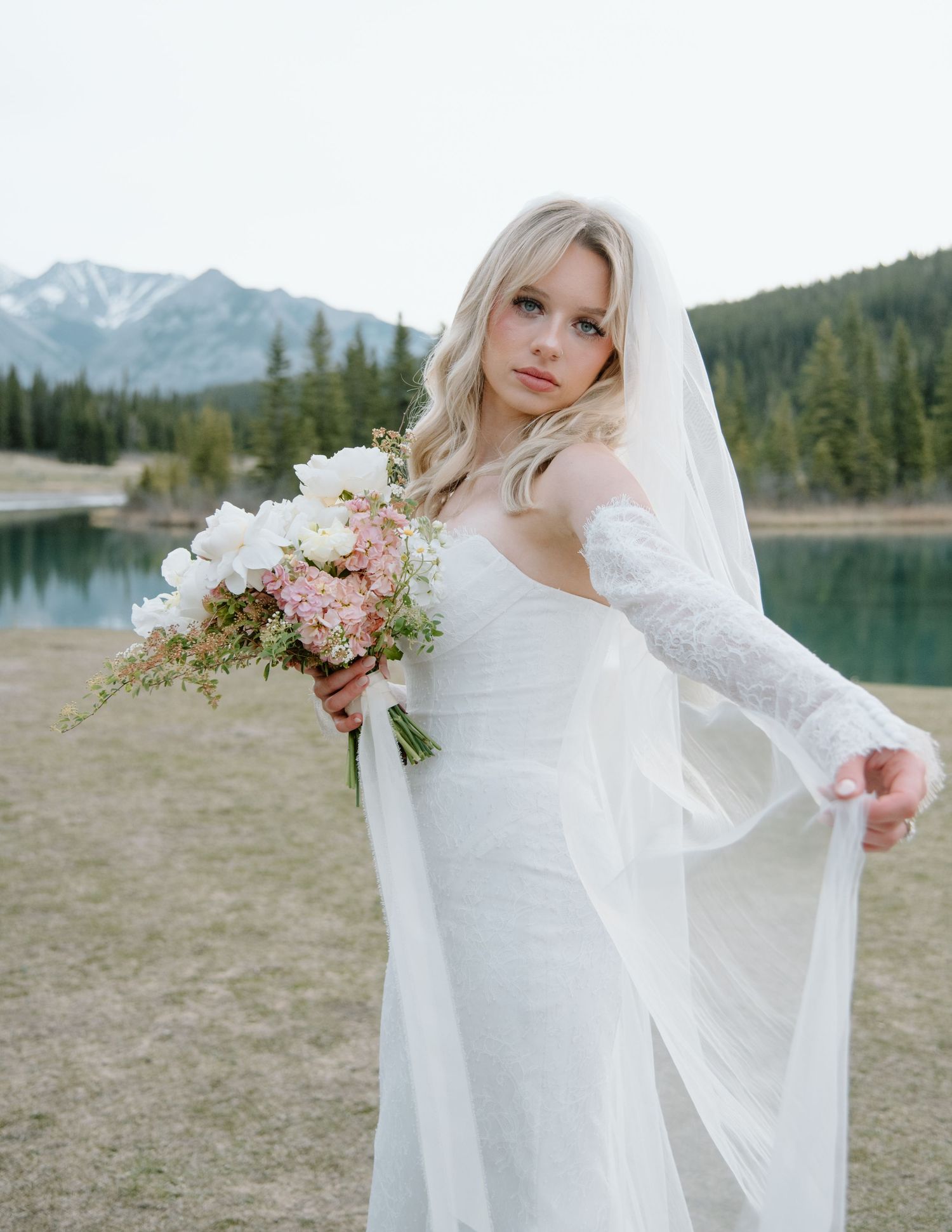 Elegant bridal portrait with flowing veil against mountain lake backdrop. Calgary Wedding Photographer