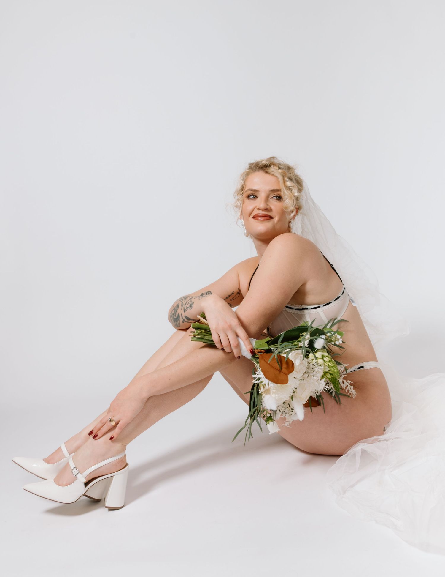 A bridal boudoir photo featuring white florals and a flowing veil against a light backdrop. Calgary Bridal Boudoir Photographer