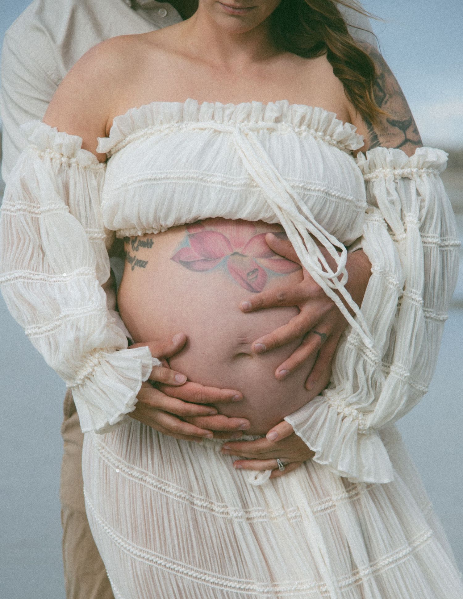 Artistic maternity photo showing a pregnant belly with hands framed by white ruffled fabric. Calgary Alberta Maternity Photographer.