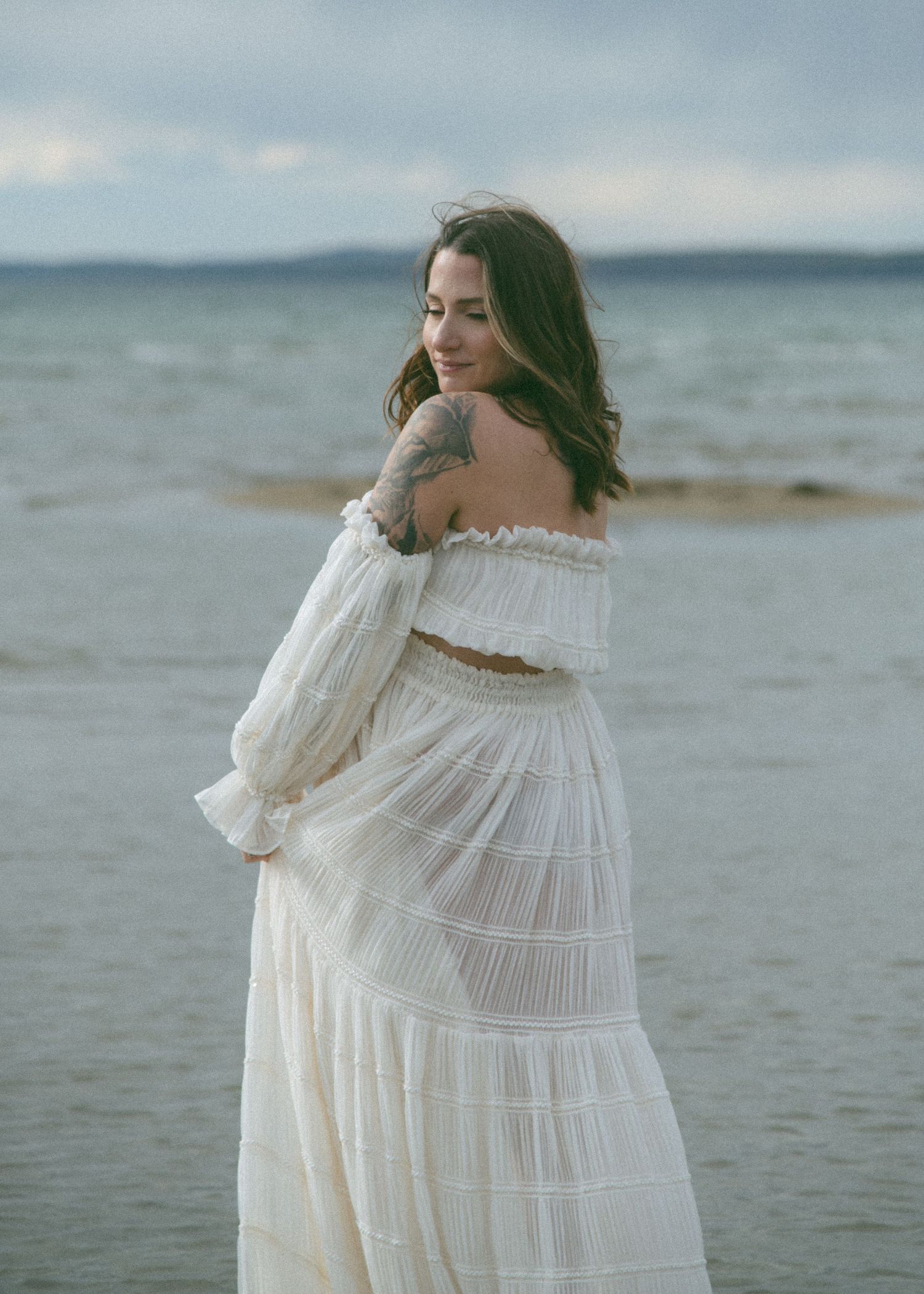 Romantic coastal photoshoot featuring a billowing white tiered dress near the water. Calgary Alberta Maternity Photographer.