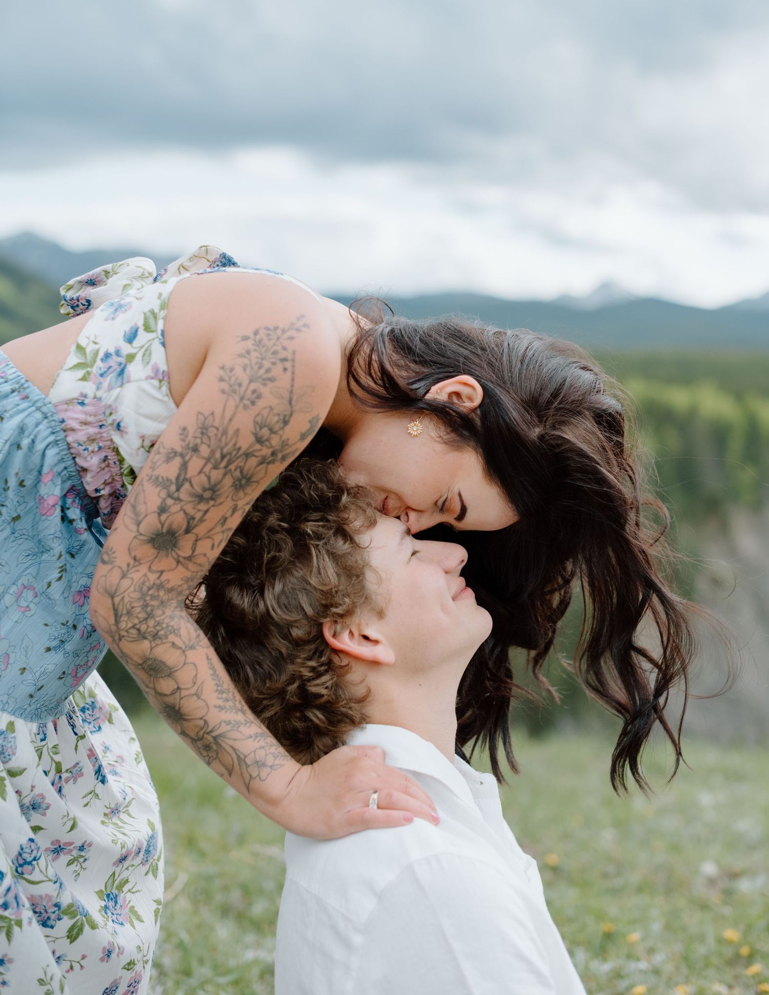 A couple sharing an intimate moment in a wildflower meadow with mountains visible. Calgary Alberta Engagement Photographer.