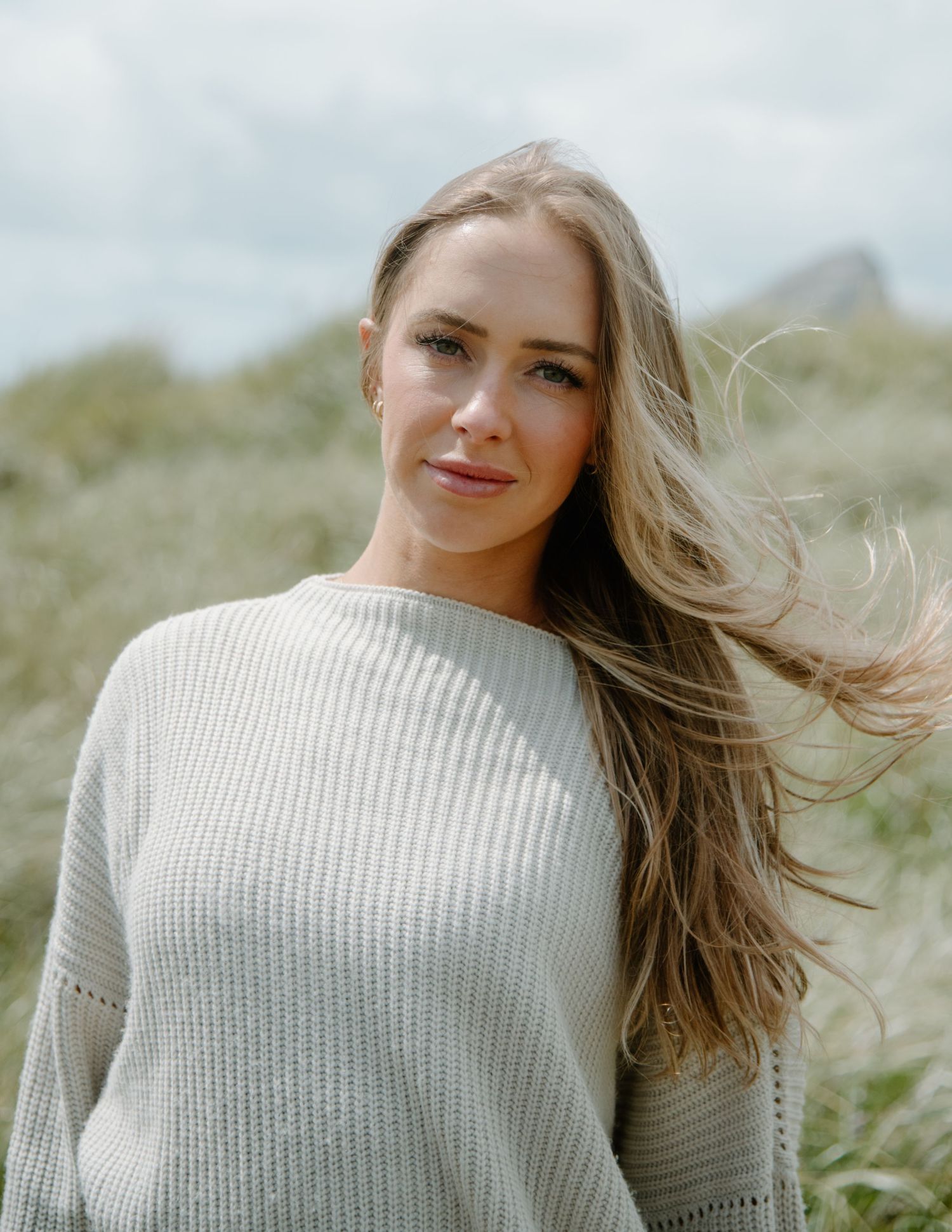 Natural light portrait featuring windswept hair and a cozy sweater against muted coastal scenery on Oregon Coast. Calgary Lifestyle.