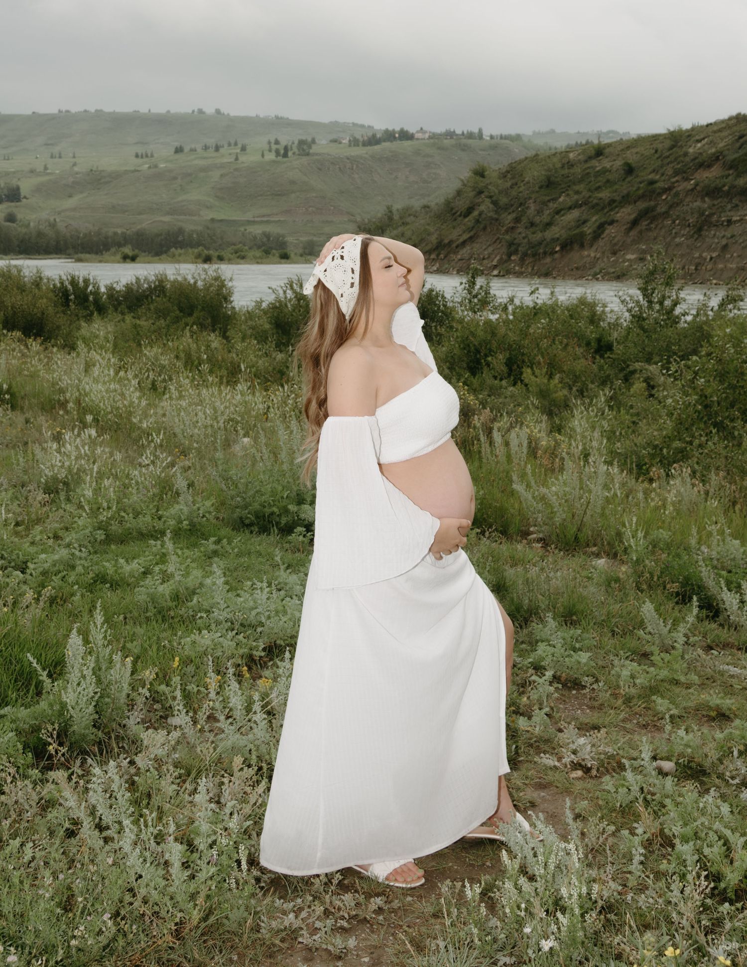 Bride in flowing white dress walks gracefully through wild sage brush in a scenic mountain meadow landscape.