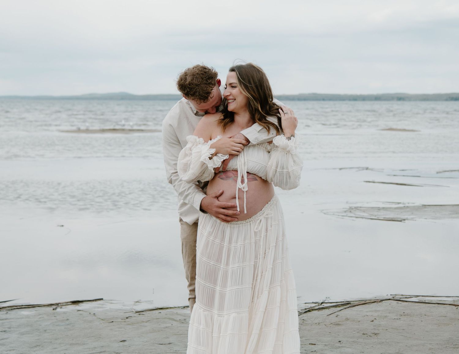 Dreamy beachside maternity photos with couple wearing white against misty backdrop. Calgary Alberta Maternity Photographer.
