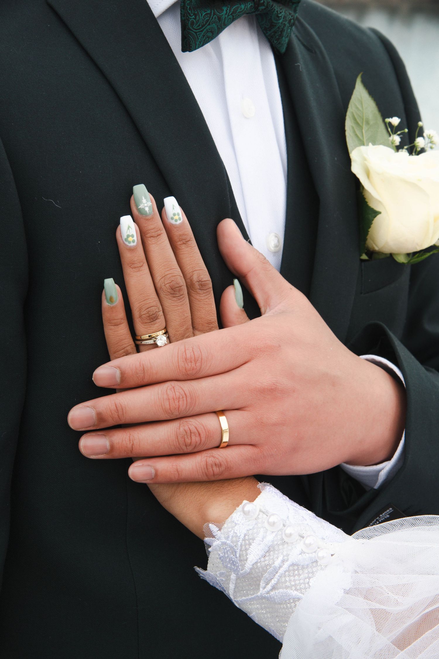 Close-up of bride and groom's hands displaying wedding rings against a formal black tuxedo. Calgary Wedding Photographer