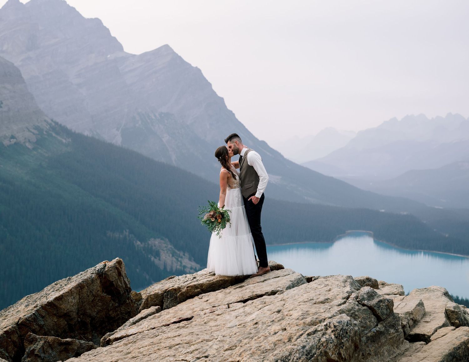 Romantic wedding moment captured on a mountain summit overlooking a turquoise alpine lake in Banff National Park.