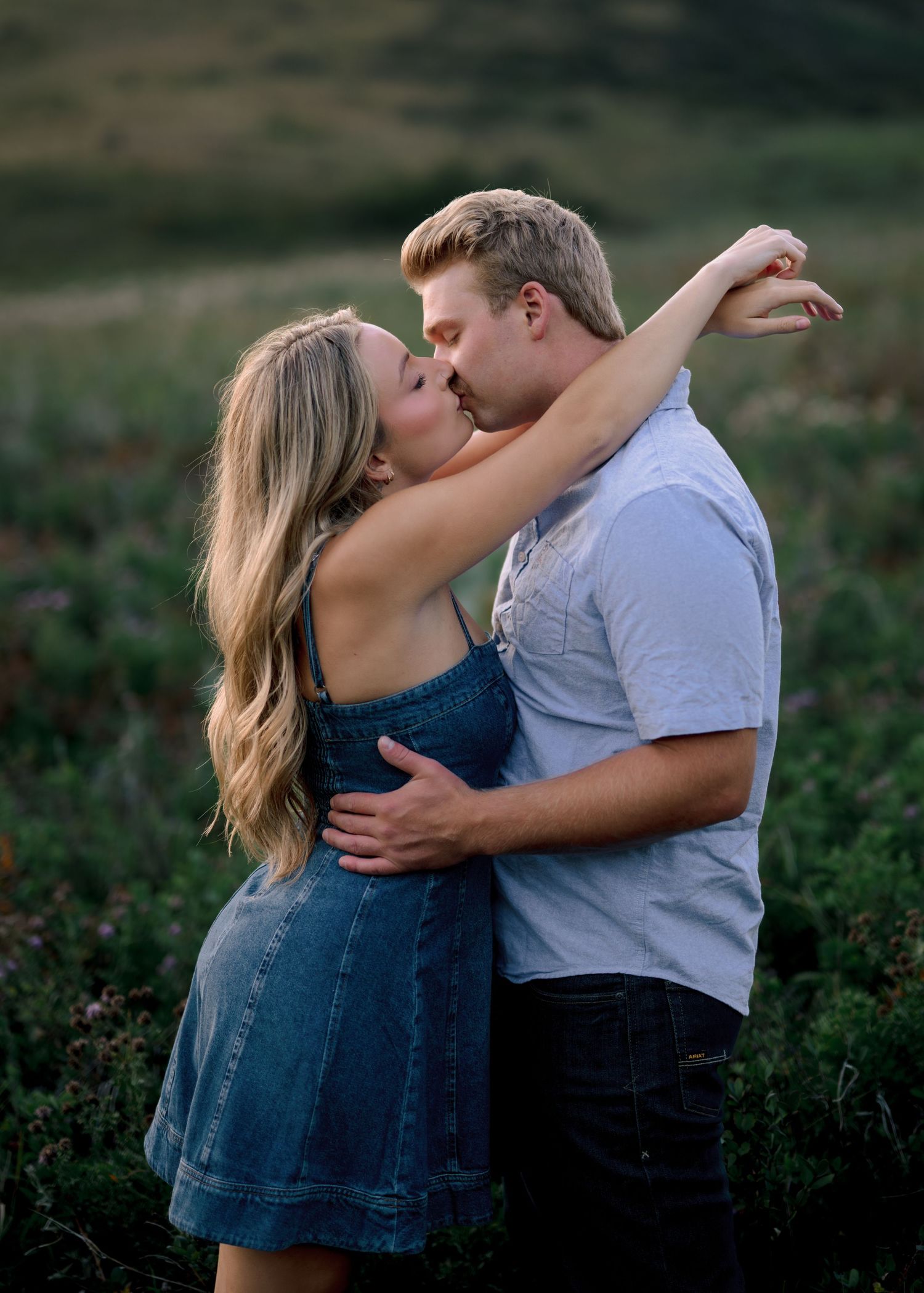A couple in a romantic embrace share a tender kiss outdoors in a natural setting at sunset.