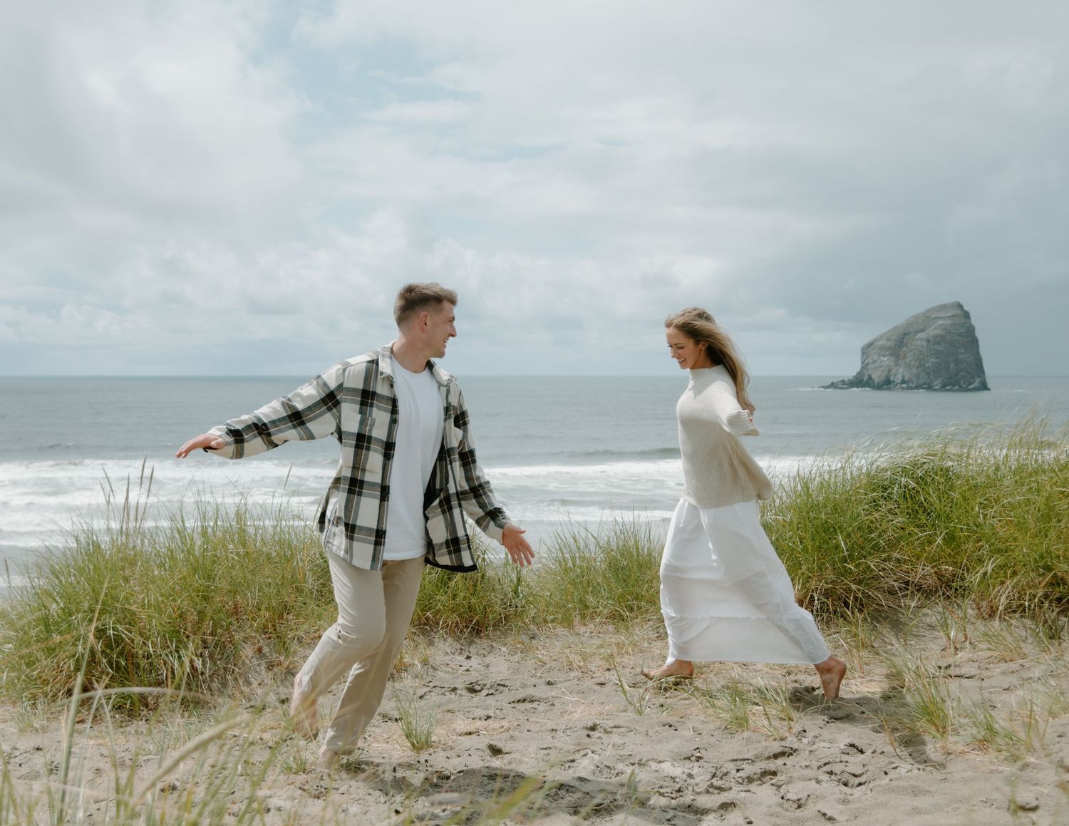 Romantic moment between couple dancing in beach grass with ocean and rock formation backdrop on Oregon Coast. Calgary Lifestyle.