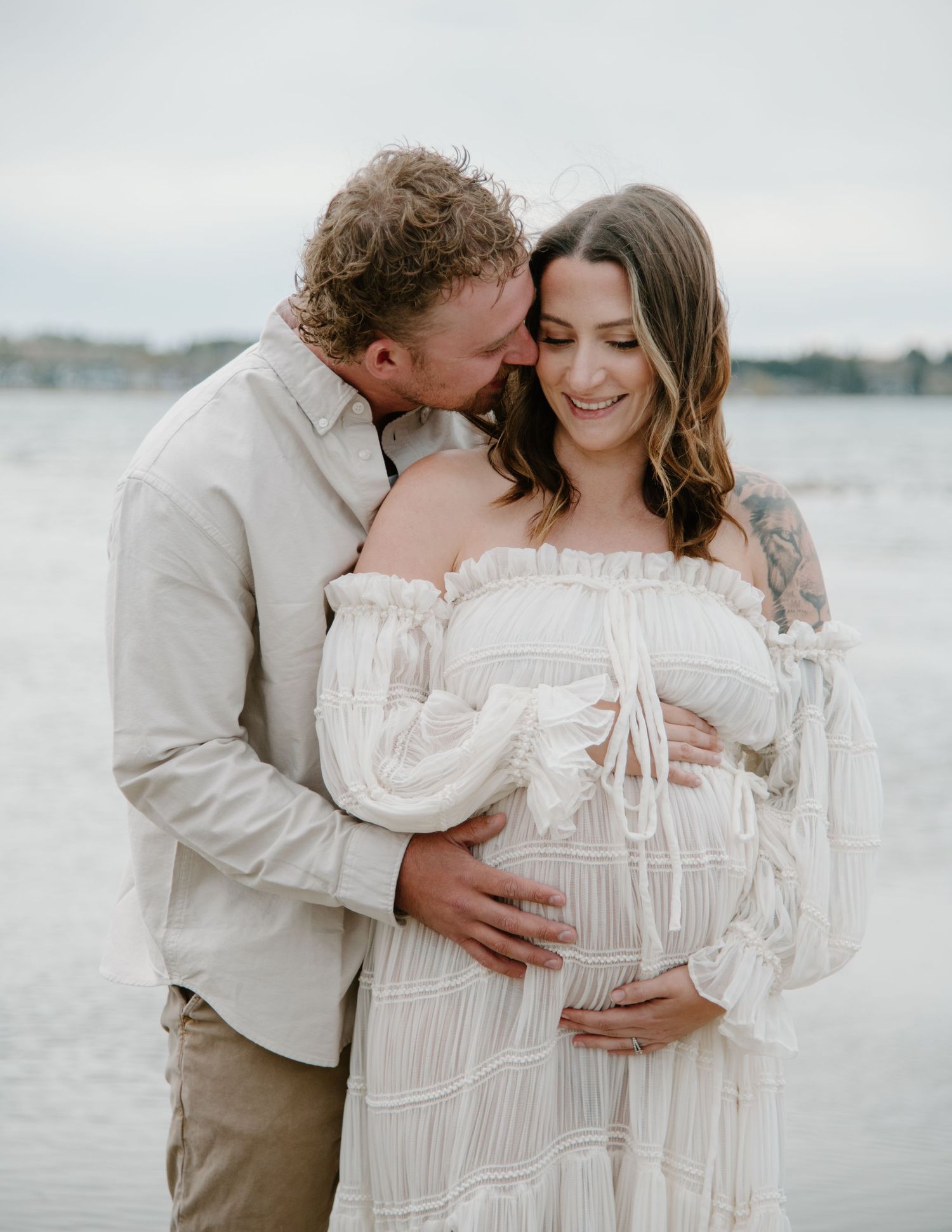 Dreamy beachside maternity session with a couple wearing white and beige against a waterfront backdrop. Calgary Alberta Maternity