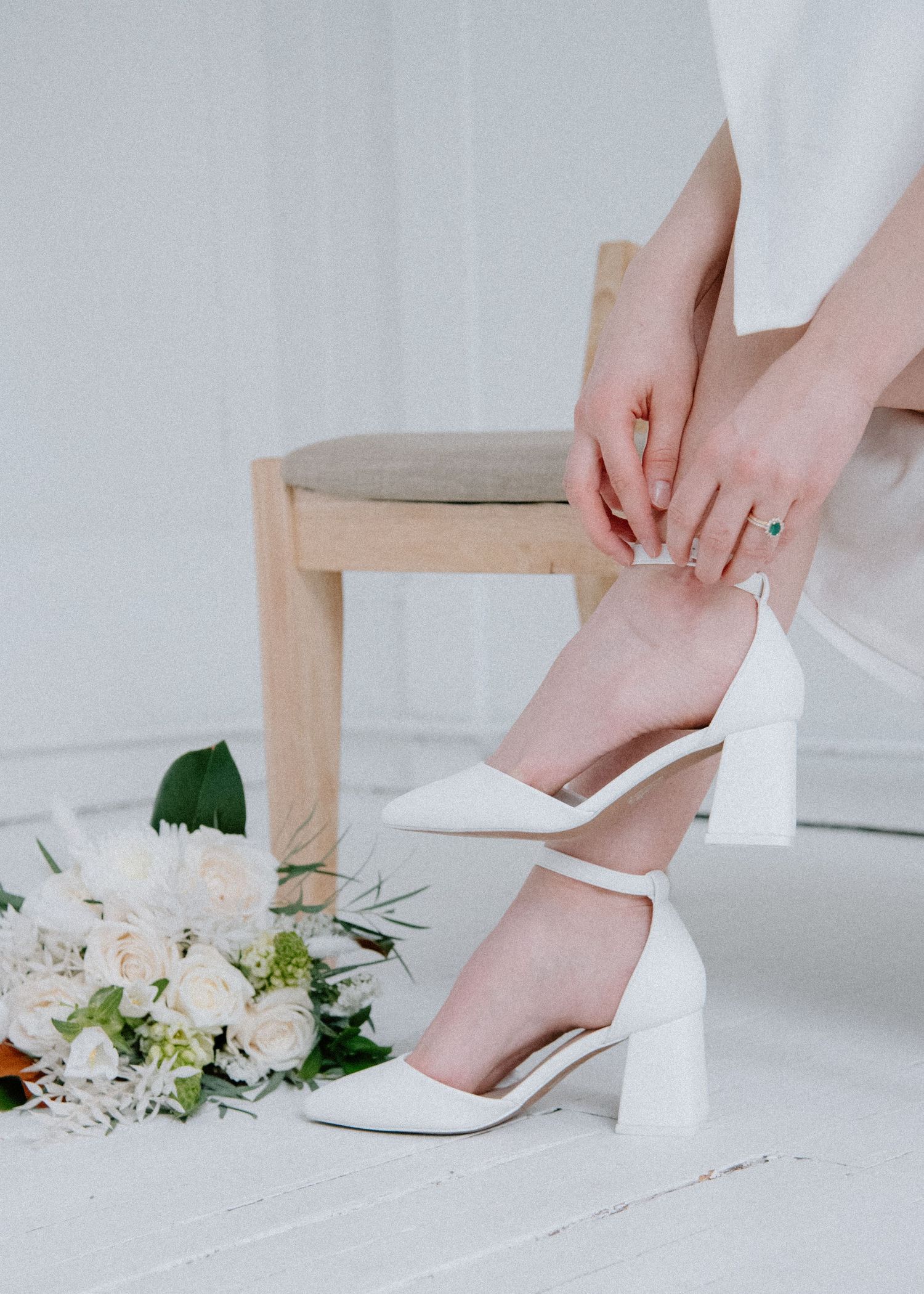 White bridal shoes being put on next to delicate floral bouquet at The Study Studios. Calgary Wedding Photographer.