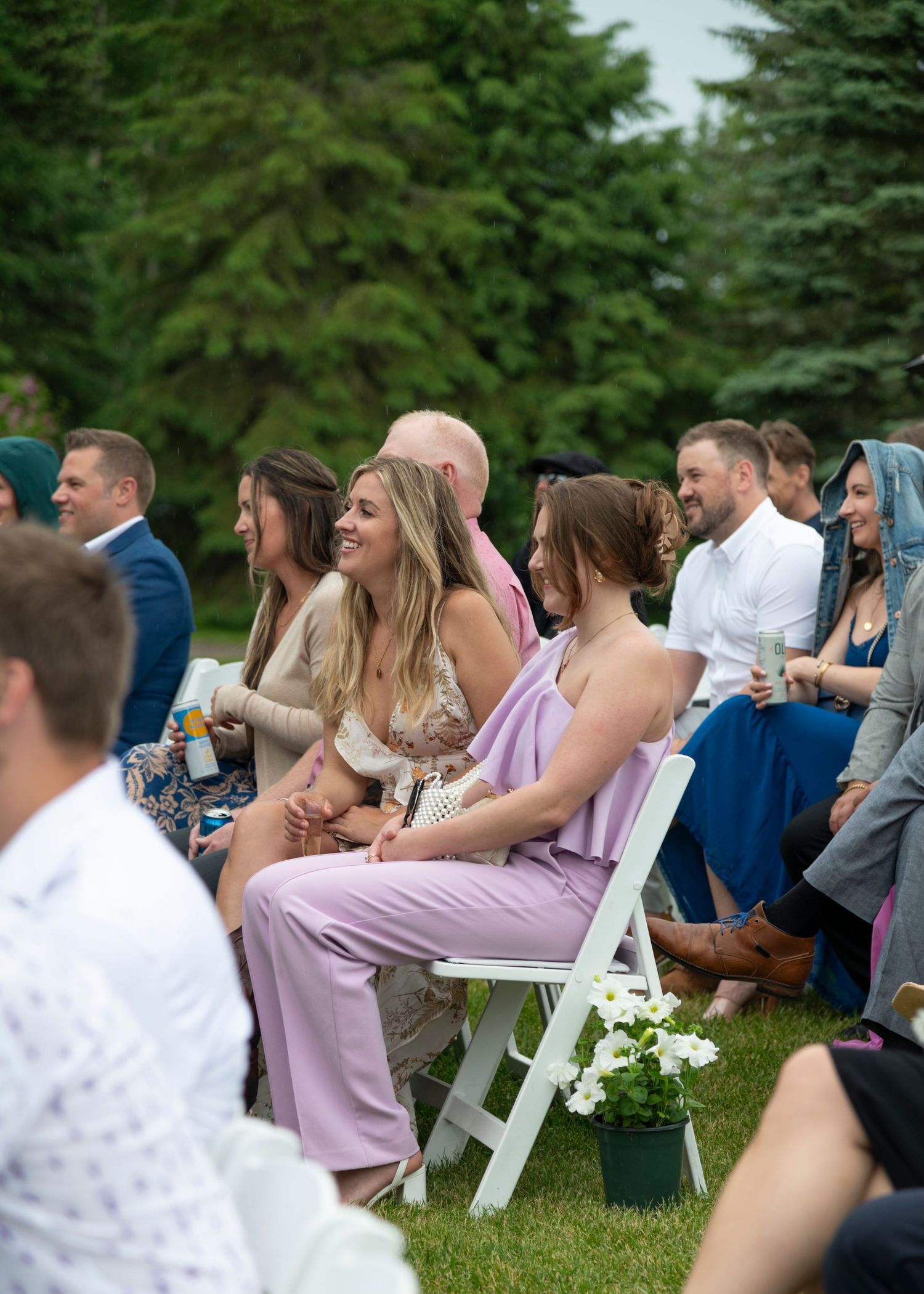 Wedding guests seated in white chairs at an outdoor ceremony surrounded by evergreen trees. Banff and Calgary Wedding Photographer