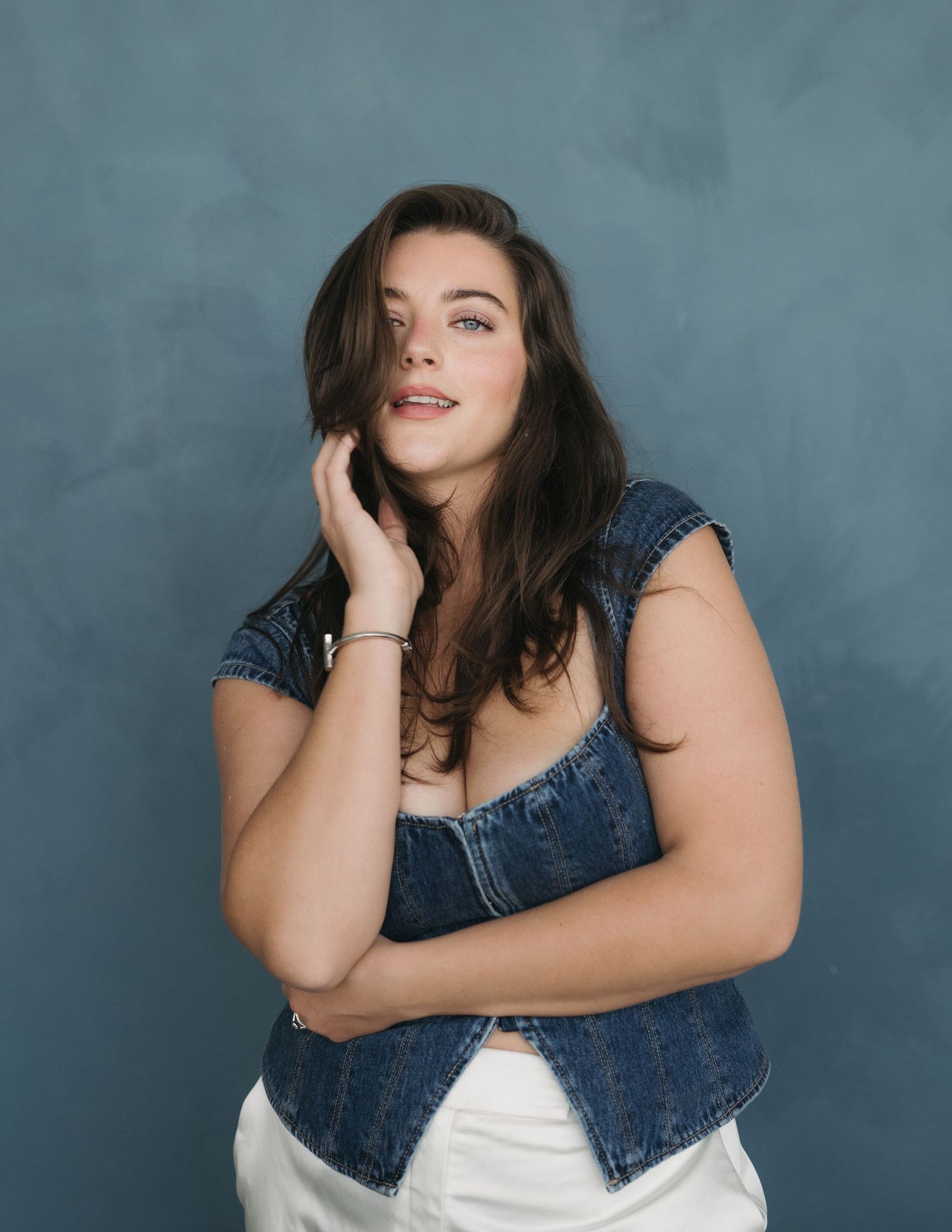 A person in a denim jacket and white dress poses against a gray backdrop in a series of candid shots.