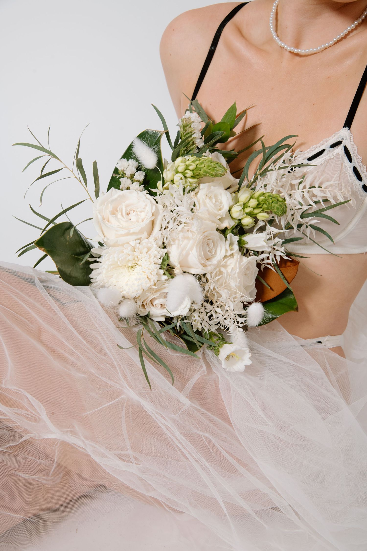An elegant white and cream bridal bouquet with roses and delicate greenery against tulle fabric. Calgary Bridal Boudoir Photographer