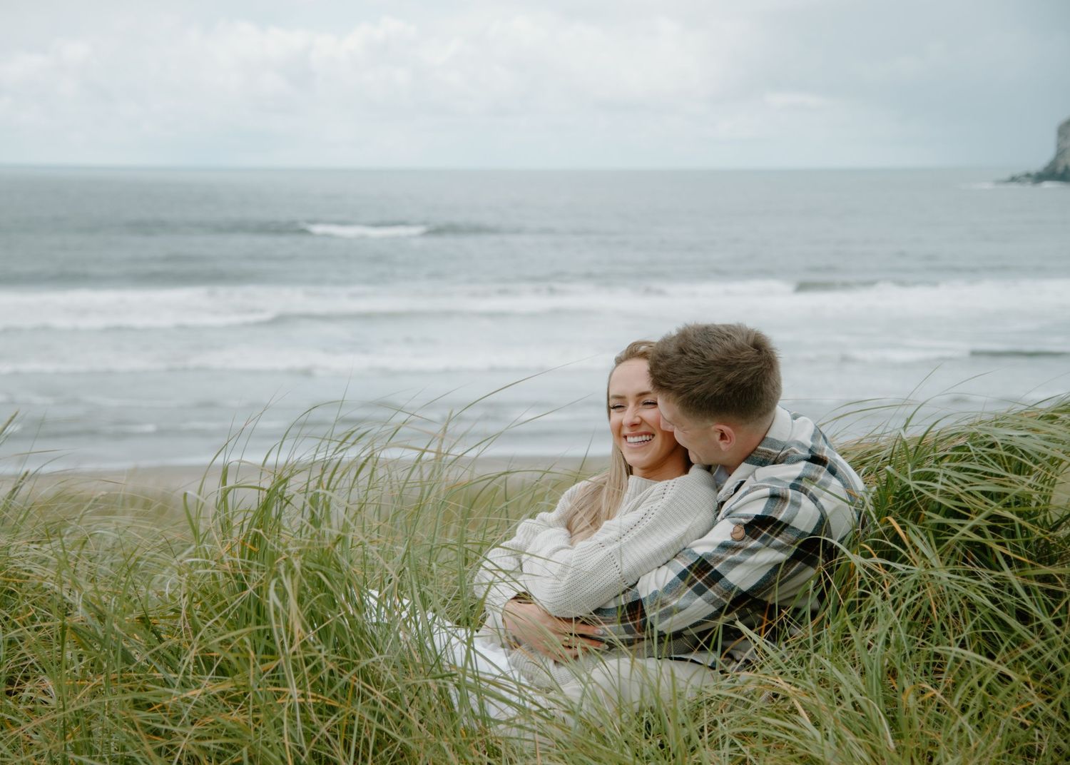 Romantic coastal photoshoot of couple nestled in beach grass overlooking the ocean on Oregon Coast. Calgary Lifestyle and Engagement.