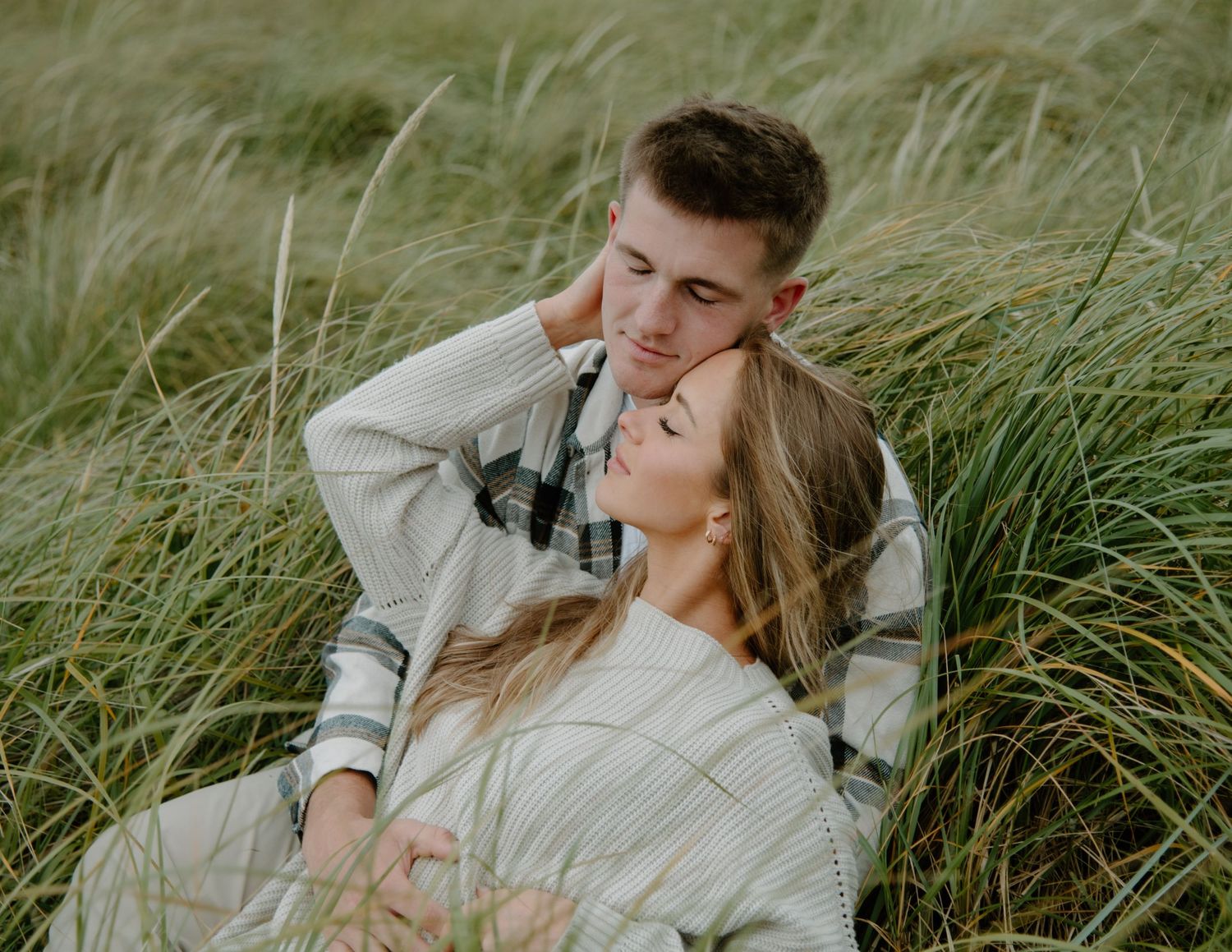 Tender moment shared on a windswept beach with dramatic coastal scenery. Calgary Alberta Engagement Photographer.