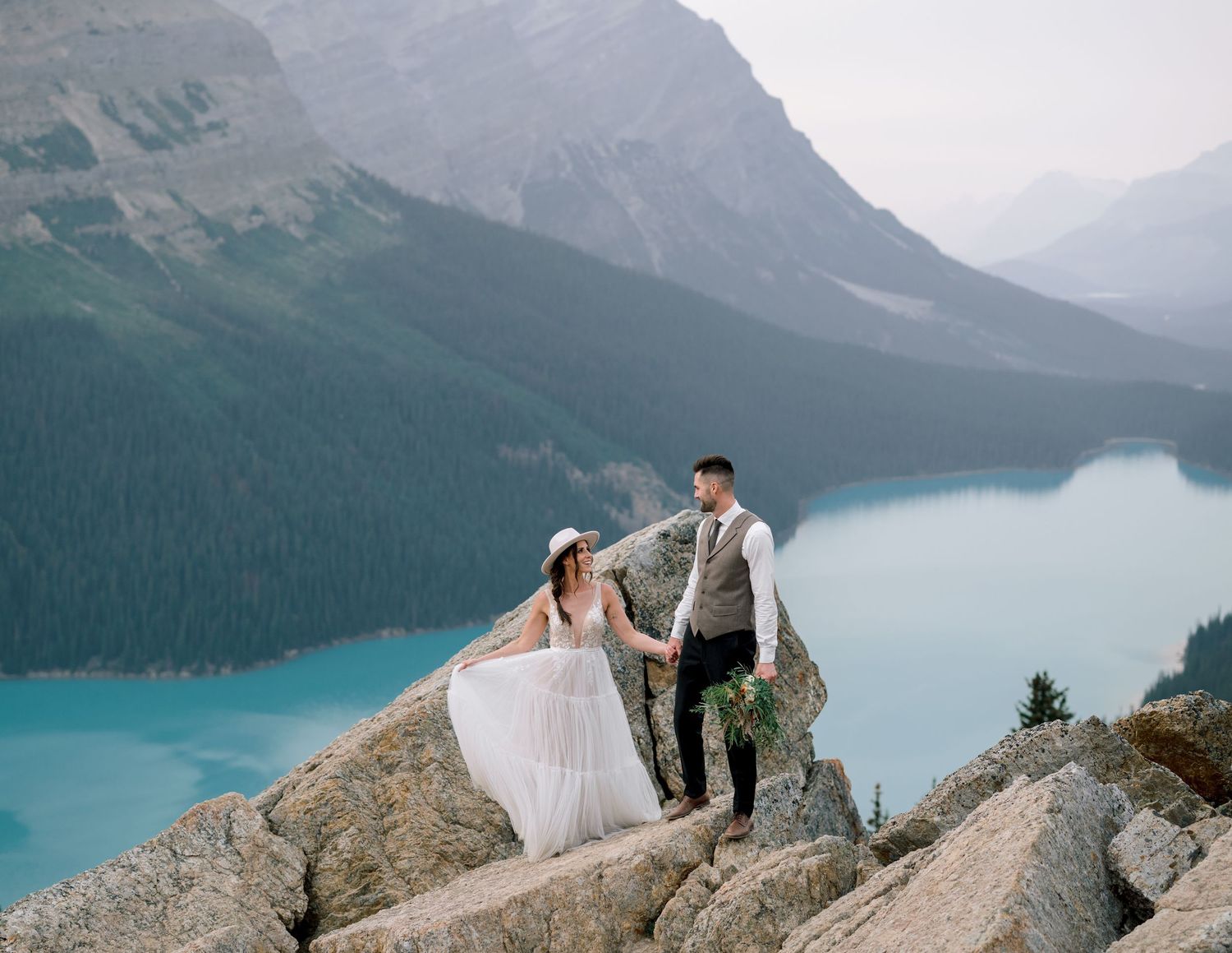 Newlyweds share a moment on a mountain ledge with the stunning turquoise waters of Peyto Lake and Canadian Rockies behind them.