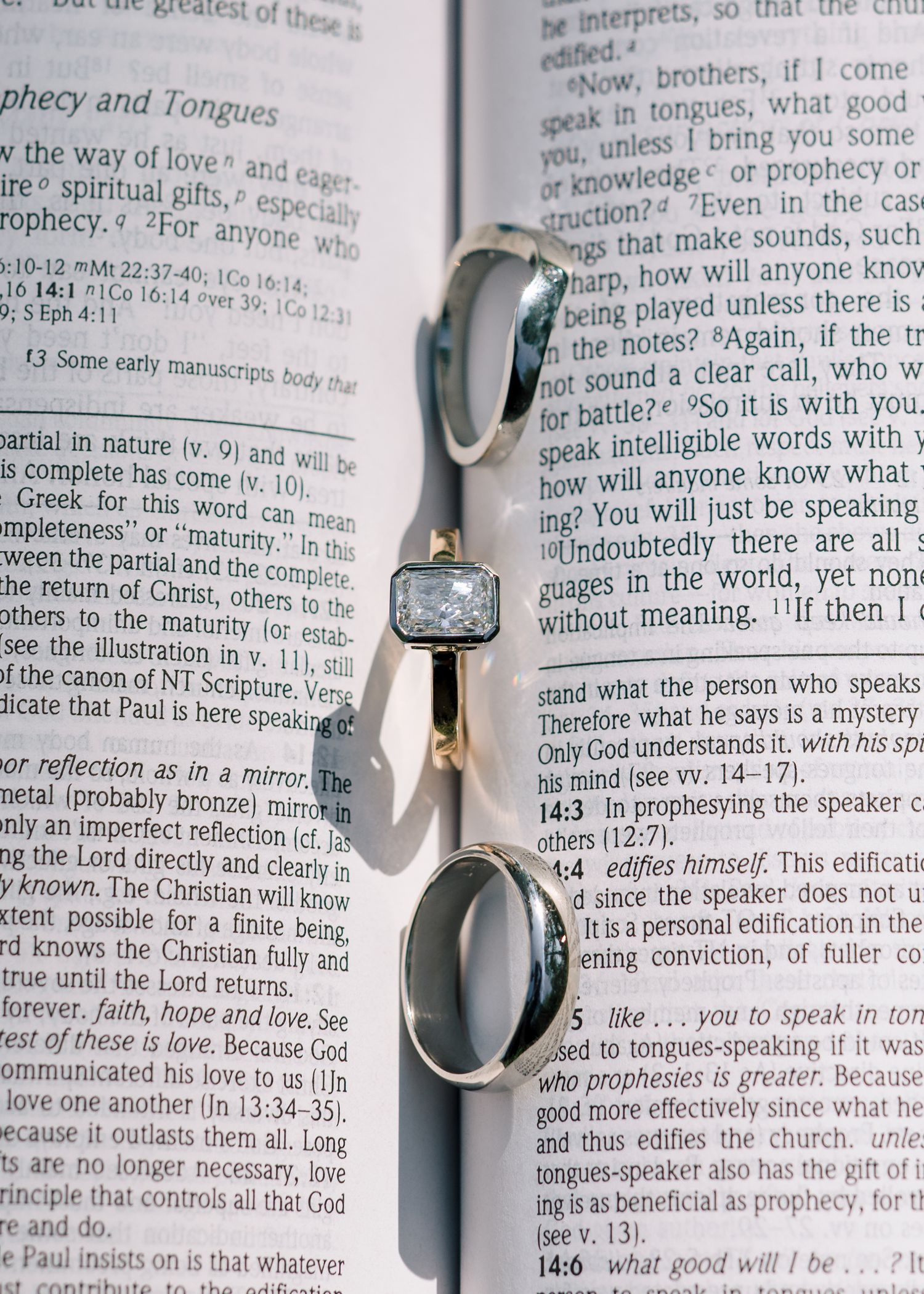 An open Bible book page lies on a wooden surface with text visible and shadows casting across the pages.