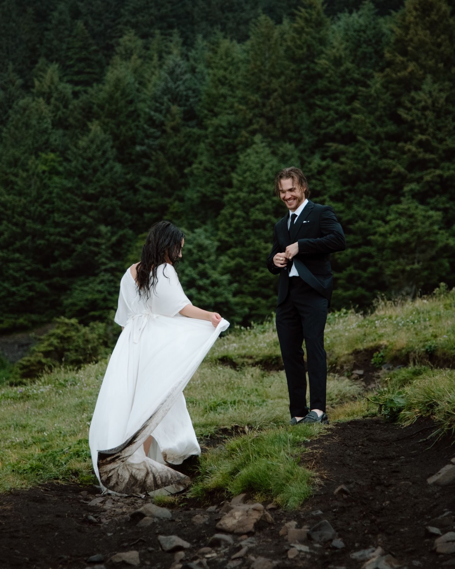 A playful wedding moment captured on a rugged mountain trail with evergreen trees in the background. Calgary Wedding Photographer