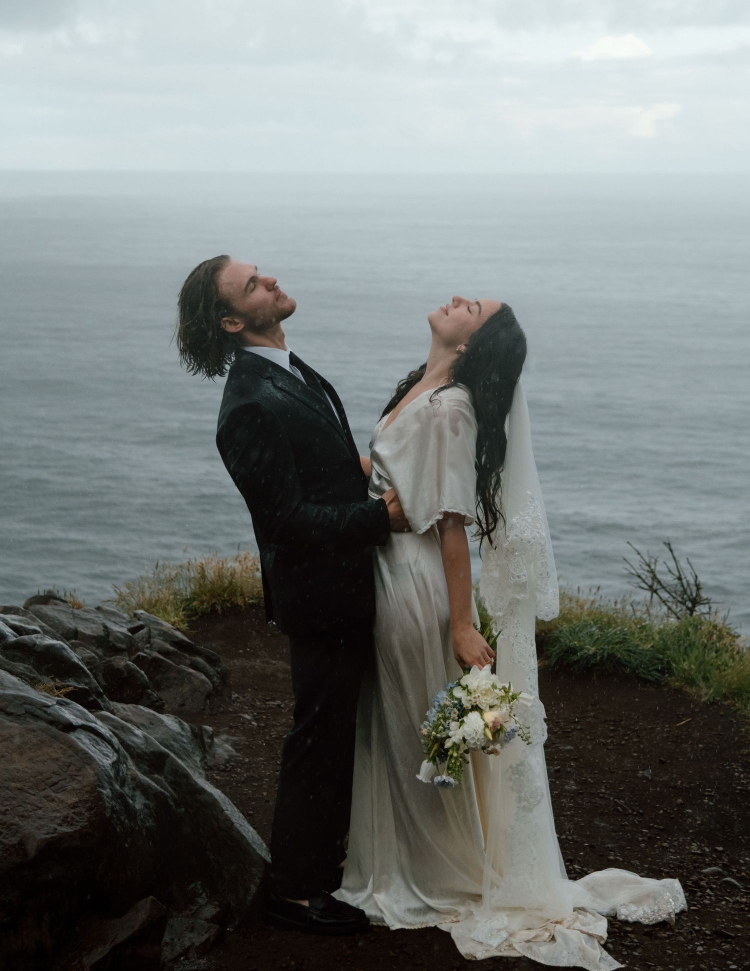 Dramatic wedding portraits captured on rocky oceanside cliff in overcast weather. Calgary Wedding Photographer