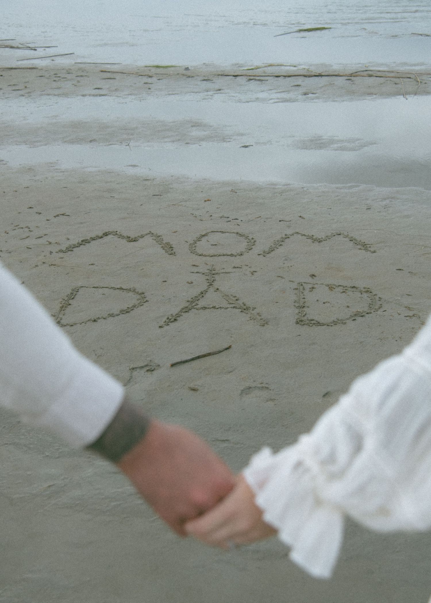 Close-up of dress hem and hands with writing in beach sand. Calgary Alberta Maternity Photographer.