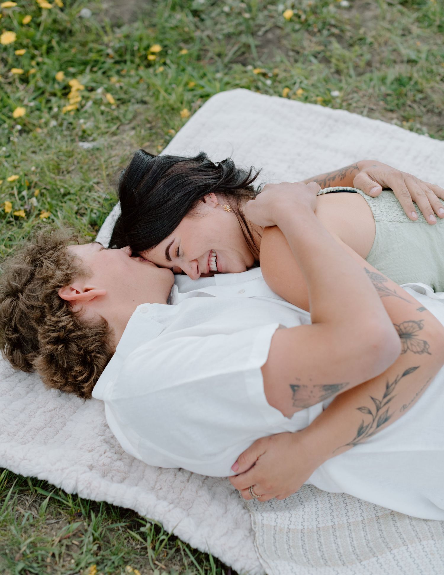A tender embrace shared on a picnic blanket surrounded by wildflowers. Calgary Alberta Engagement Photographer.
