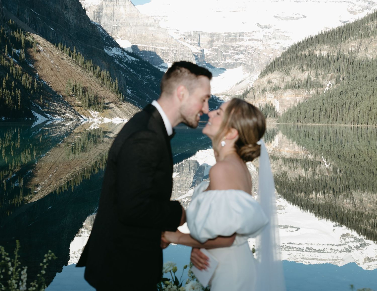 A couple shares a romantic moment at Lake Louise with snow-capped mountains and turquoise waters in the background.