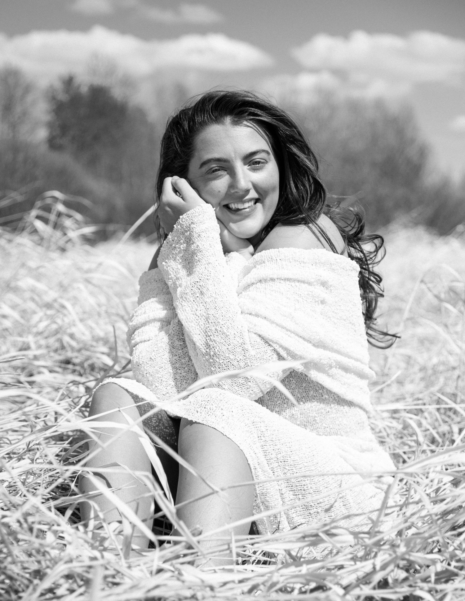 Black and white portrait of a person laying in grass with a cozy sweater on a sunny day. Calgary Branding Photographer