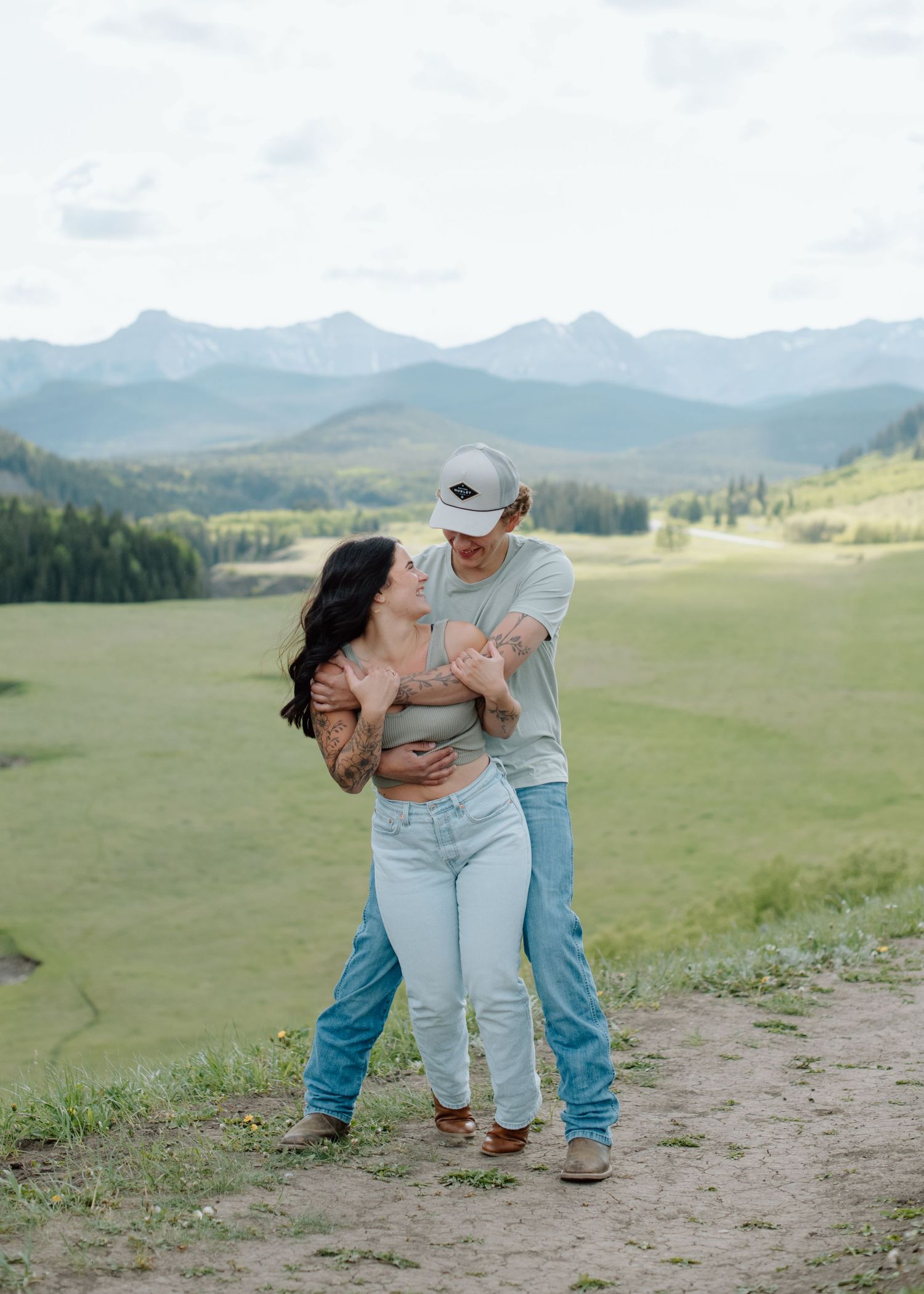 Two people sharing a playful moment against a backdrop of mountain peaks. Calgary Alberta Engagement Photographer.