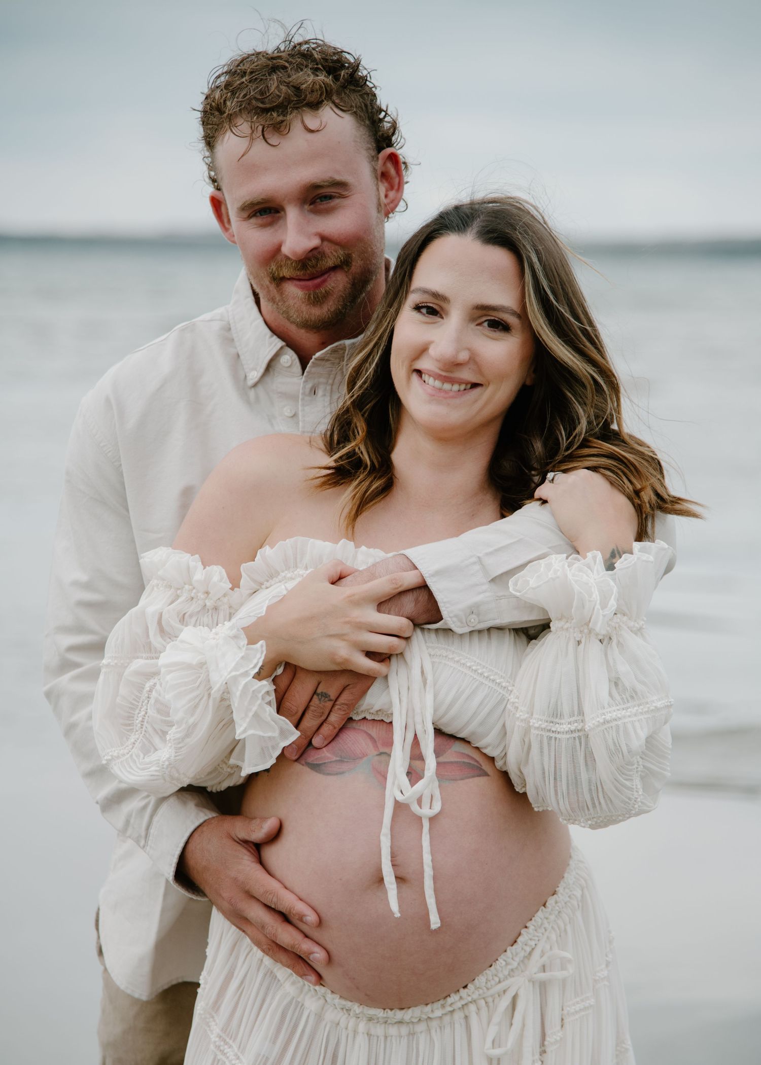 Candid maternity beach portraits showing loving couple in ethereal white attire. Calgary Alberta Maternity Photographer.