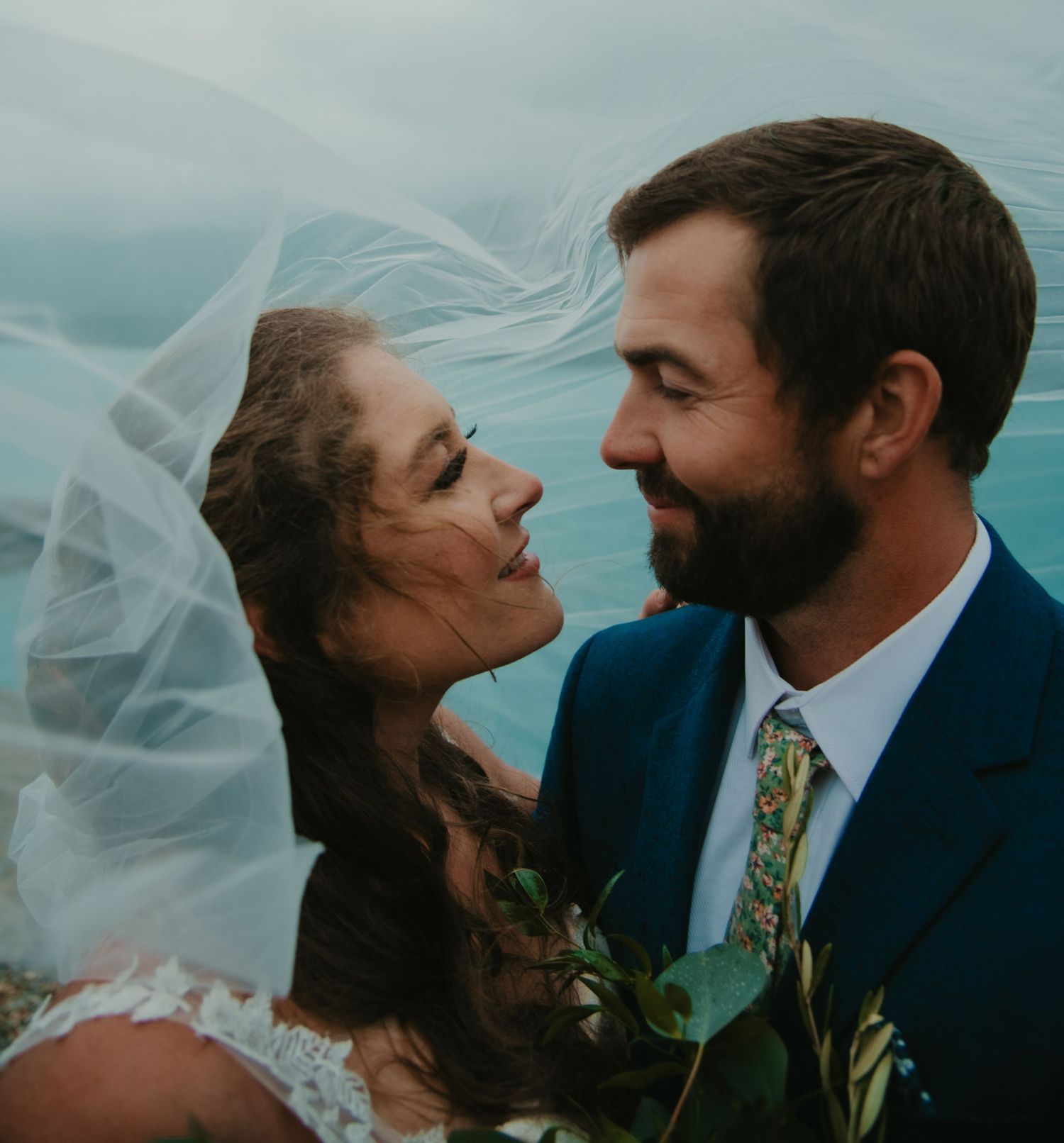 Intimate moment between couple against turquoise water backdrop with flowing veil. Banff and Calgary Wedding Photographer
