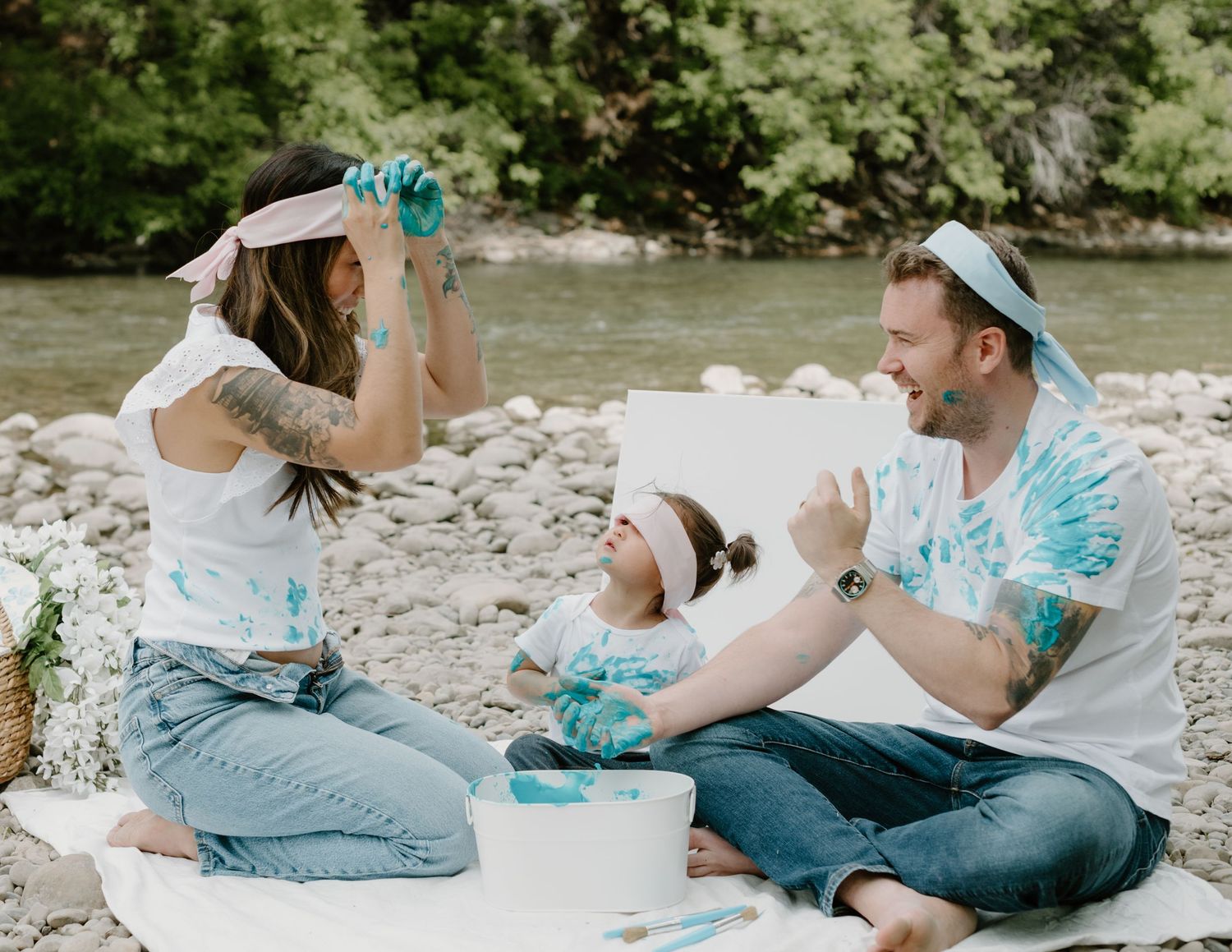 A family plays with blue paint while sitting on a blanket by the river. Calgary Alberta Family and Maternity Photographer.
