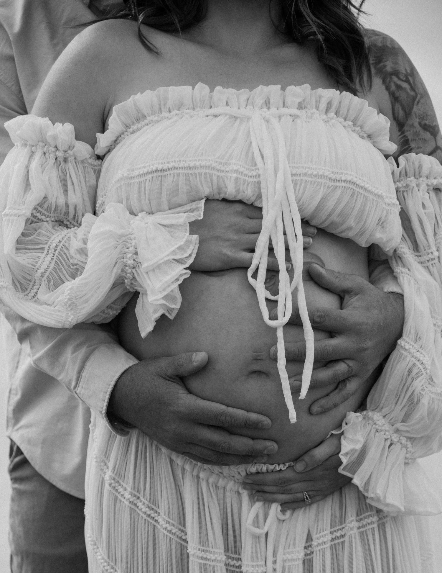 Black and white intimate maternity photo showing hands cradling a pregnant belly in lace dress. Calgary Alberta Maternity Photographer.