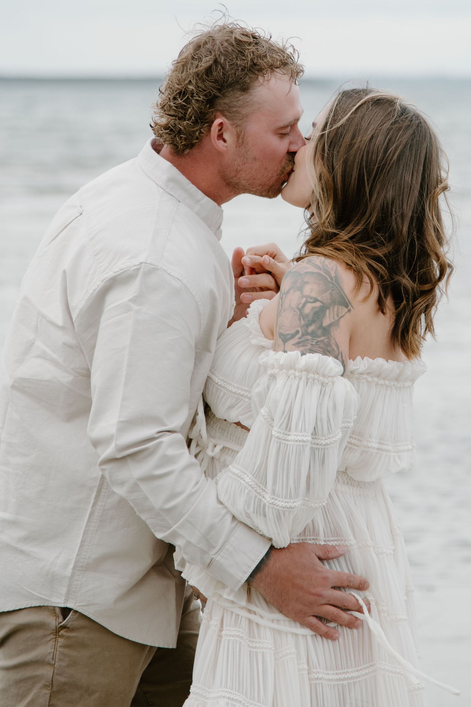 An intimate beach portrait of a couple sharing a romantic kiss by the ocean. Calgary Alberta Maternity Photographer.
