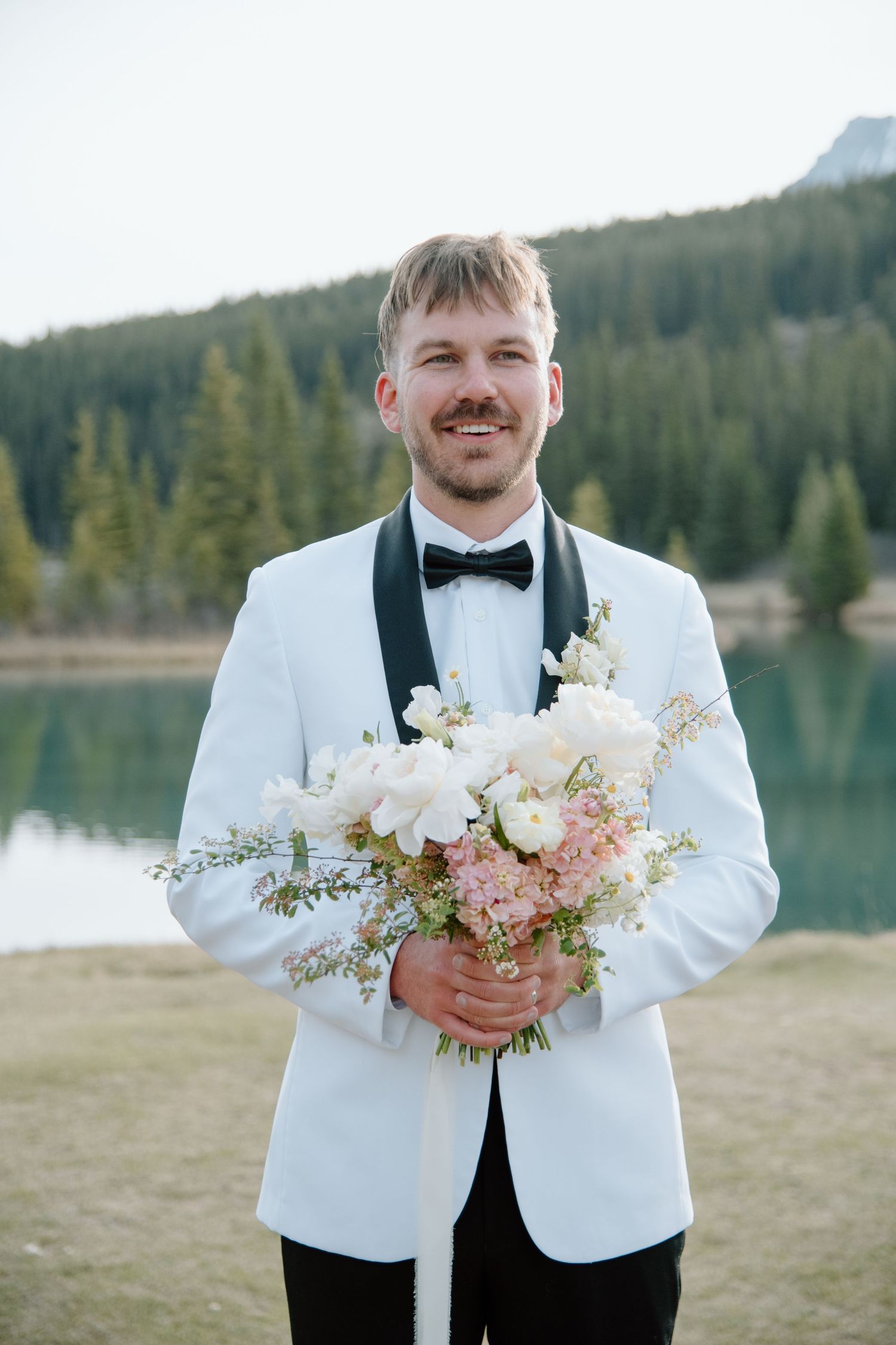 Wedding attire details showing white tuxedo jacket and delicate floral bouquet. Calgary Wedding Photographer