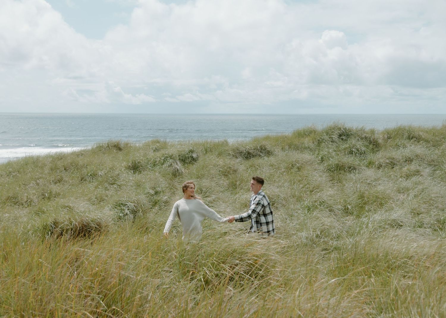 Panoramic view of coastal dunes with tall grass and cloudy sky over the ocean. Calgary Alberta Engagement Photographer.