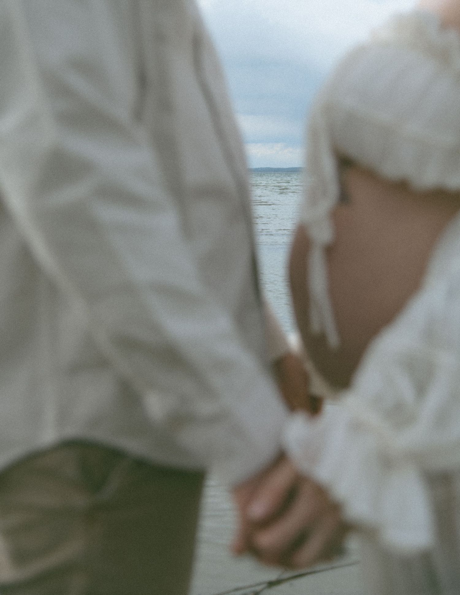 Artistic blurred close-up of couple holding hands by the water. Calgary Alberta Maternity Photographer.
