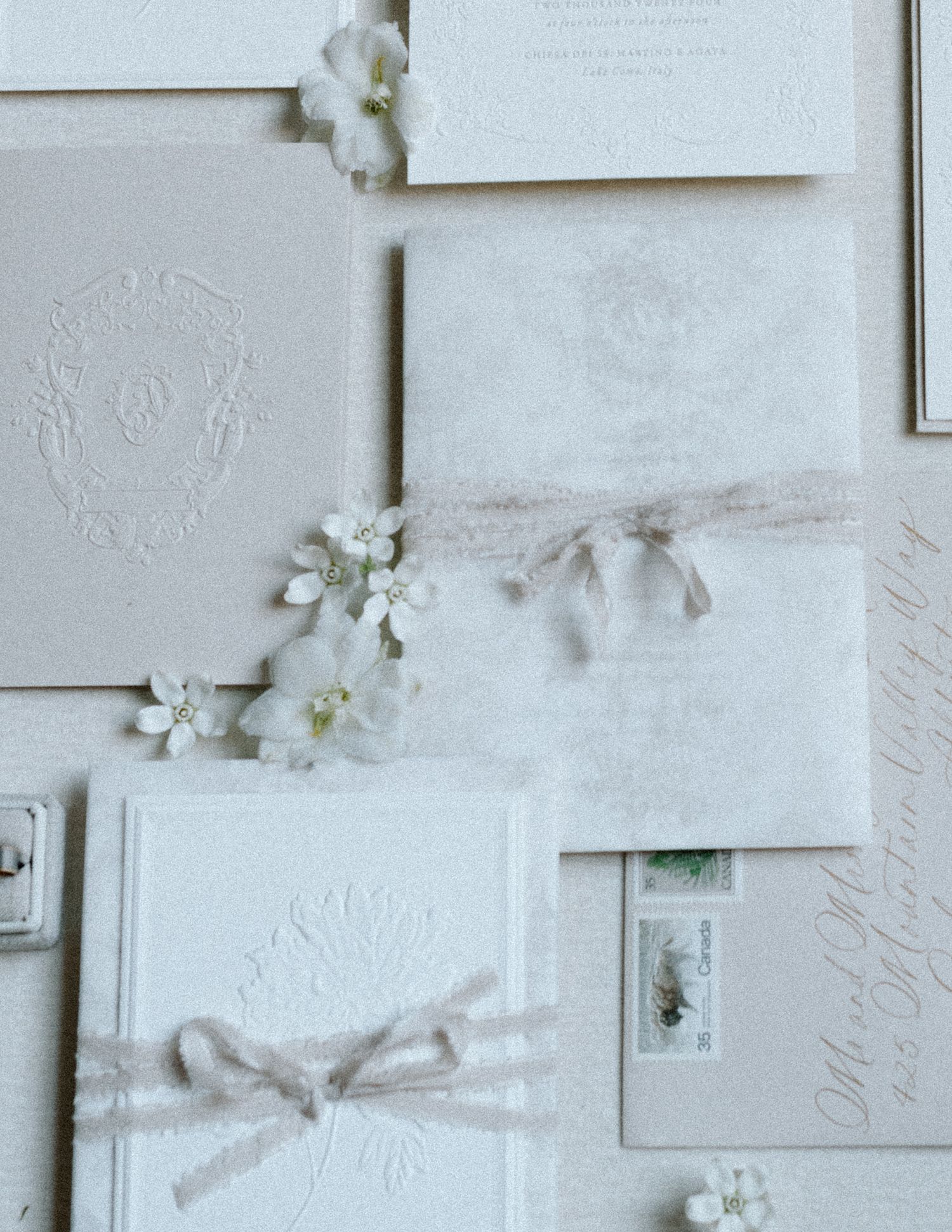 White wedding stationery and delicate flowers arranged on a textured light grey background. Calgary Wedding Photographer