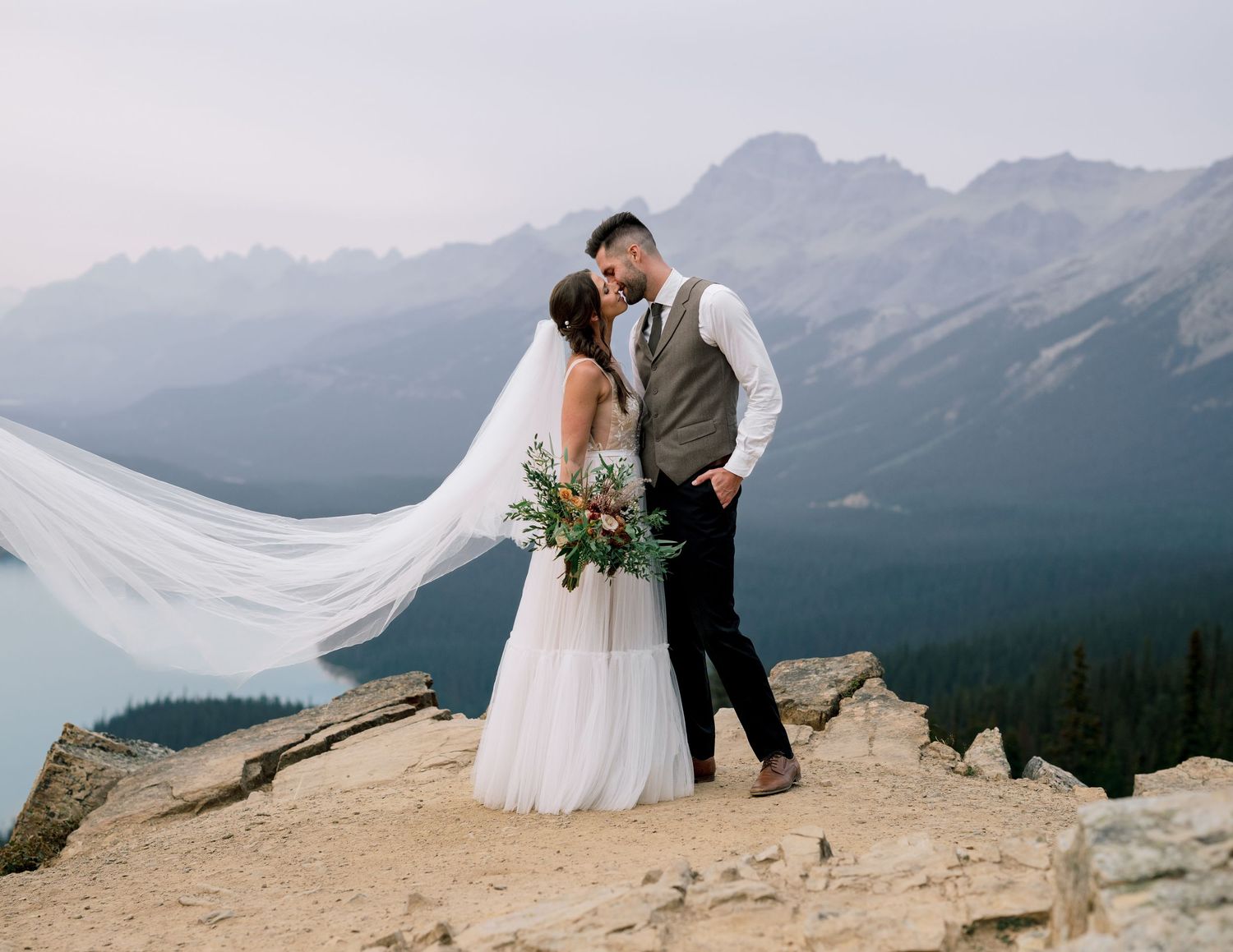 A wedding photoshoot captures intimate moments of a couple on a scenic mountain peak with dramatic views.