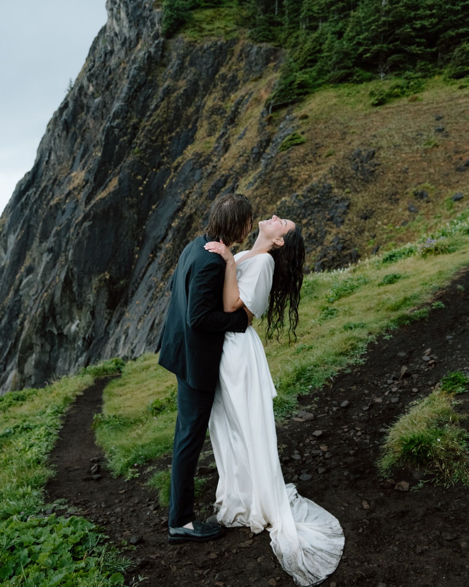 A romantic wedding portrait against a dramatic coastal cliff face with moody overcast skies. Calgary Wedding Photographer