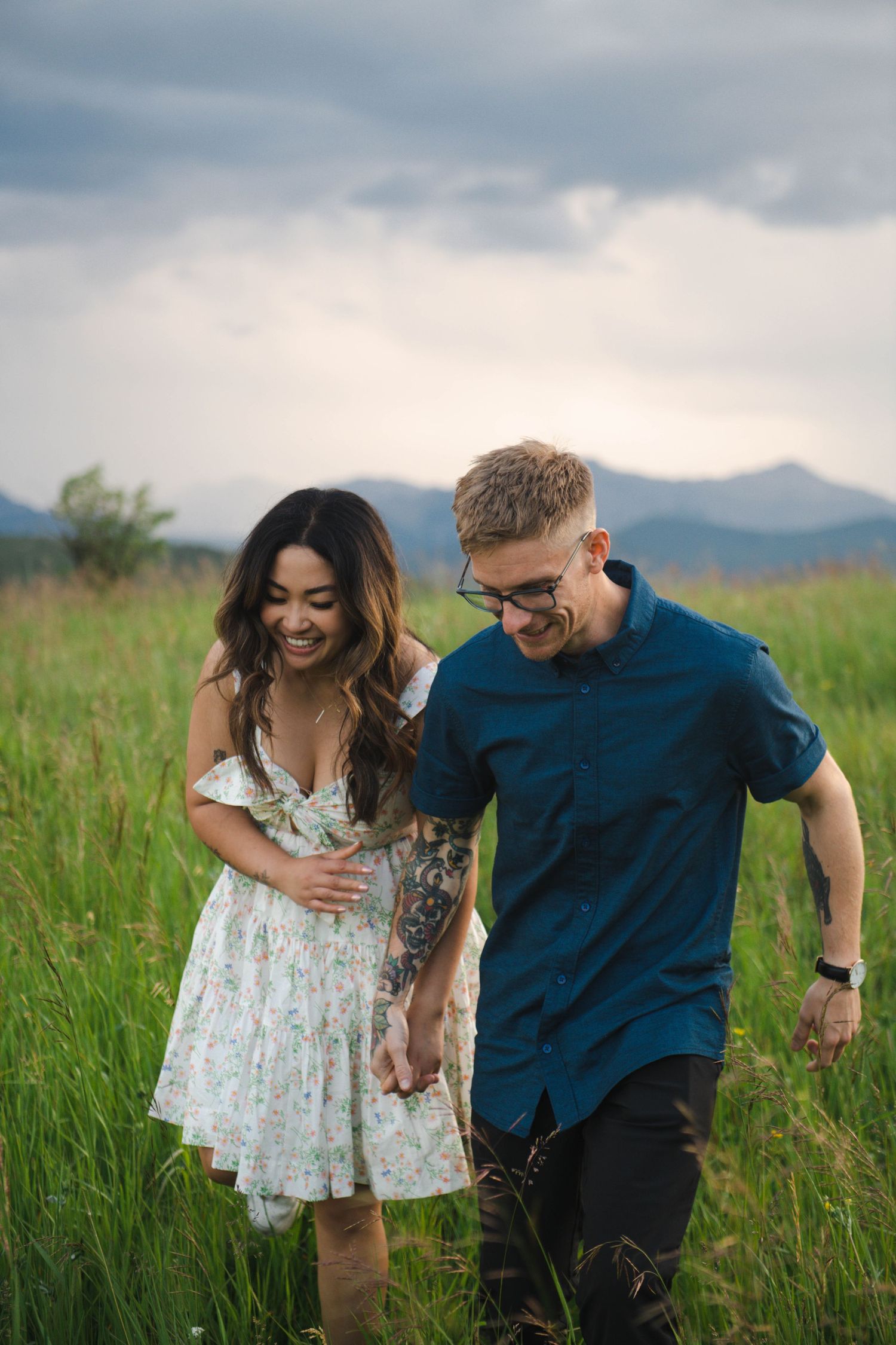 A couple laughs together while walking through a lush mountain meadow in Calgary. Calgary Lifestyle and Engagement Photographer.