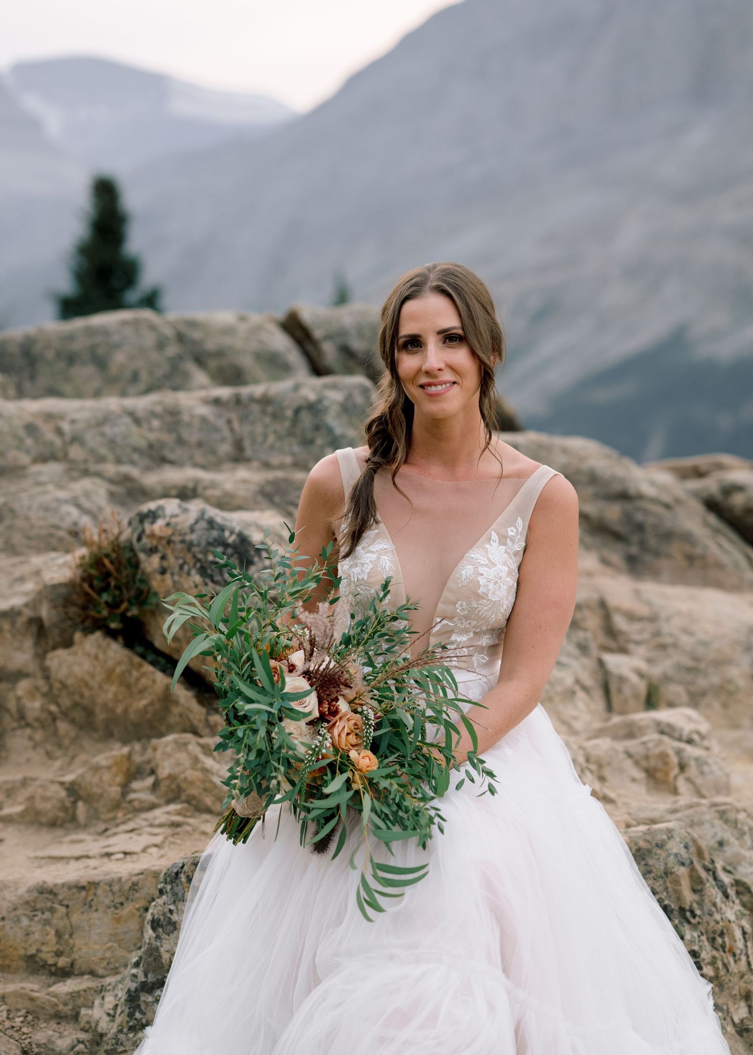 Wedding photoshoot overlooking Peyto Lake features white dress and natural greenery bouquet against mountain backdrop.