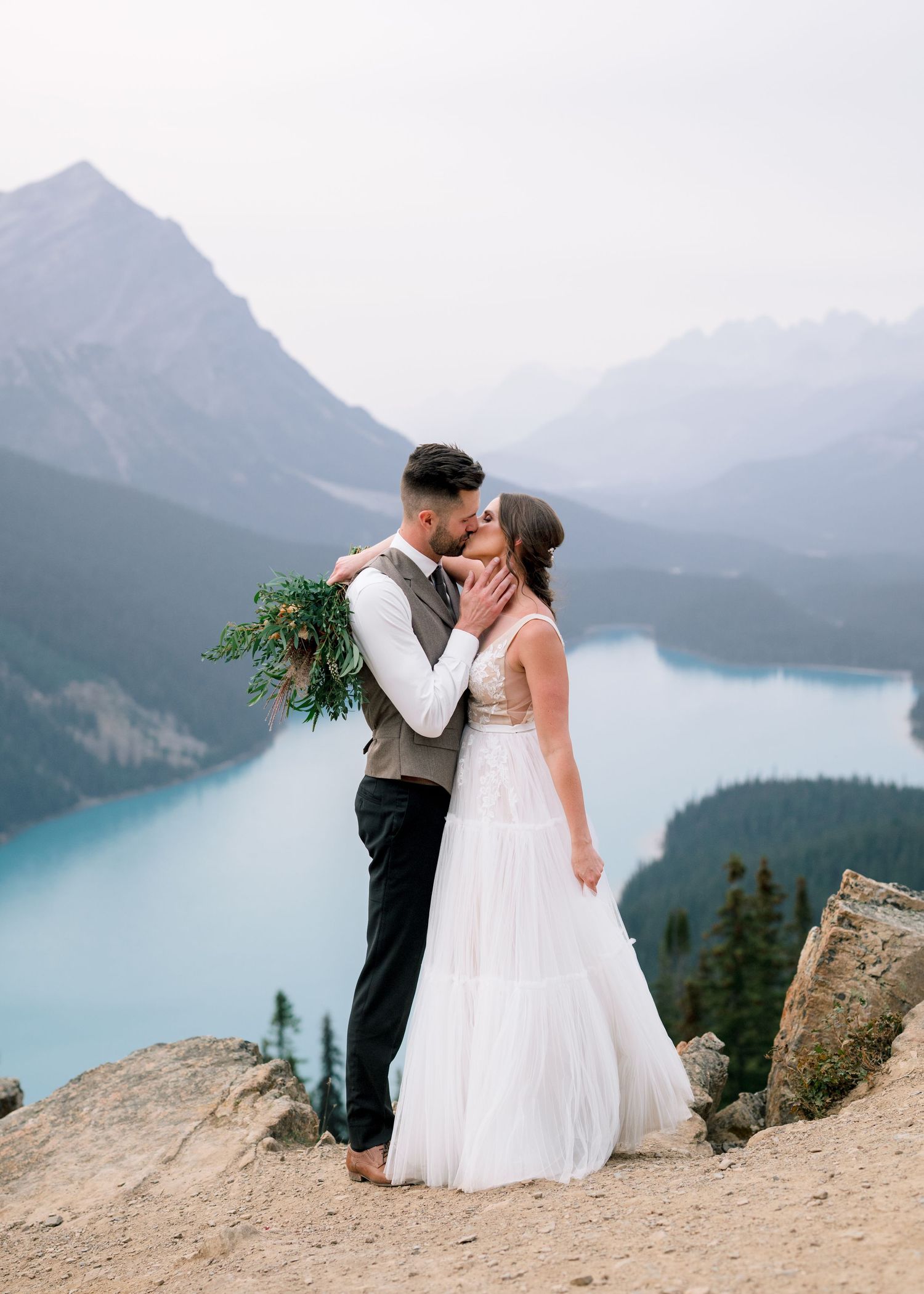 A couple shares a romantic moment at Peyto Lake viewpoint in Banff National Park with turquoise waters and mountains behind them.