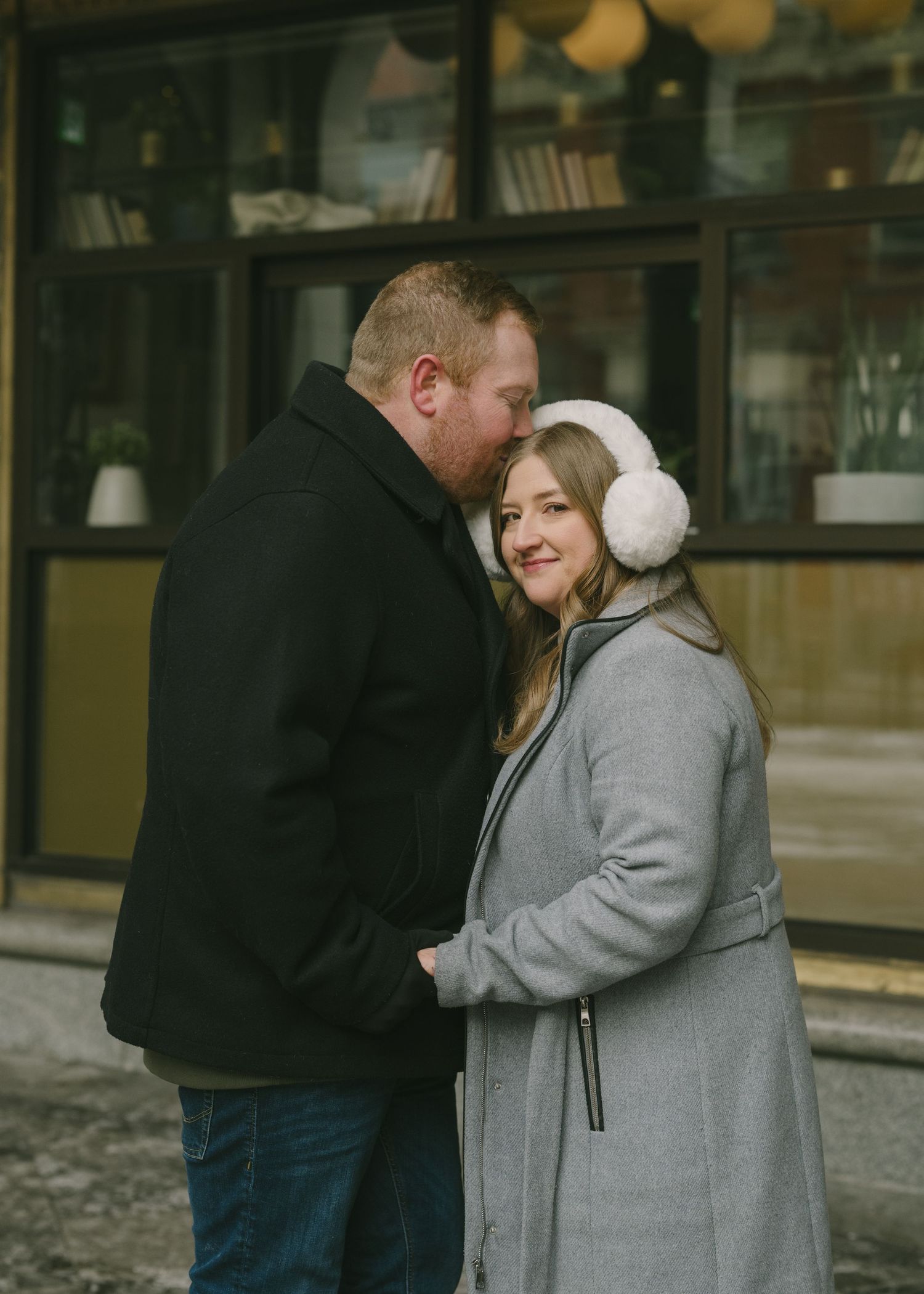 A couple in winter attire embraces on a snowy city street, sharing a tender moment together.