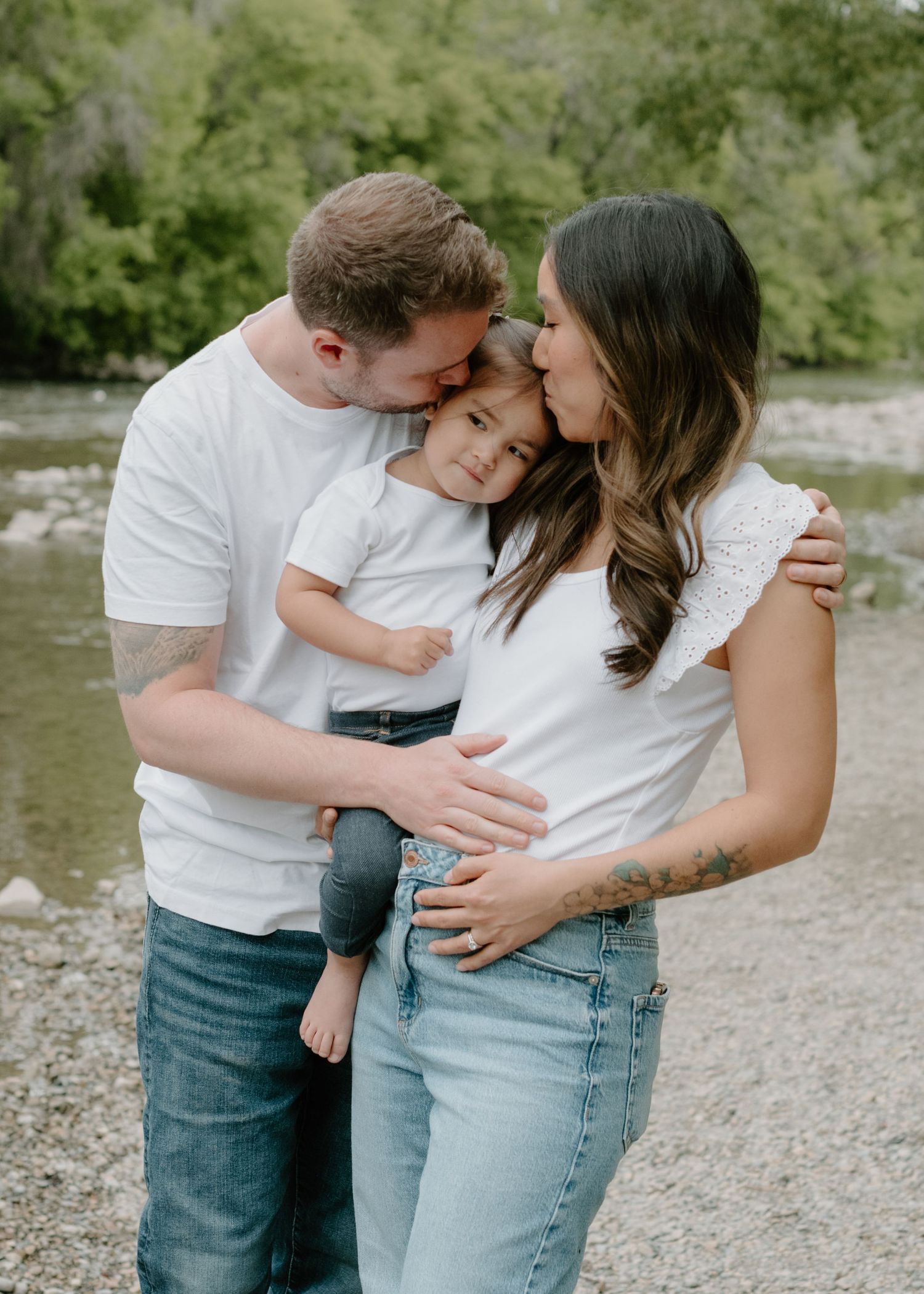 A family shares an intimate moment of affection together by a riverside Calgary Alberta Family and Maternity Photographer.
