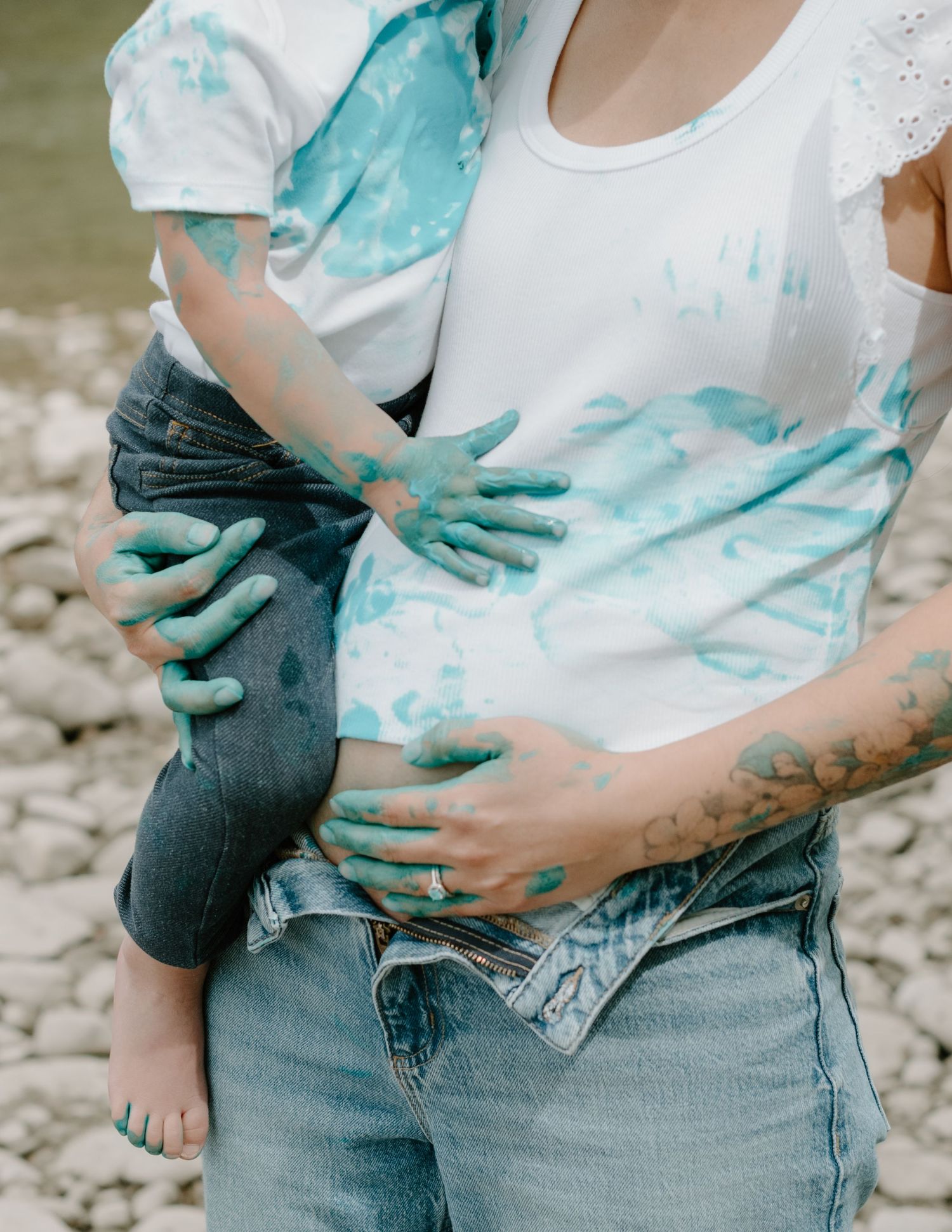 Teal and white paint stains cover clothing as hands create messy art during an outdoor photoshoot. Calgary Alberta Maternity Photographer